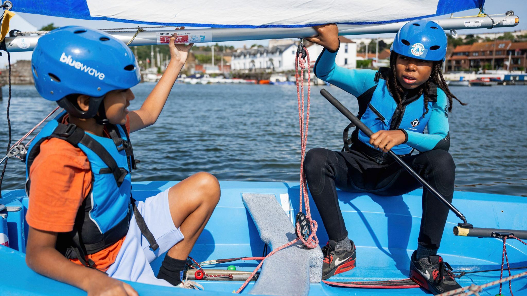 Two young boys in blue life jackets and helmets, sitting on a blue boat on the river