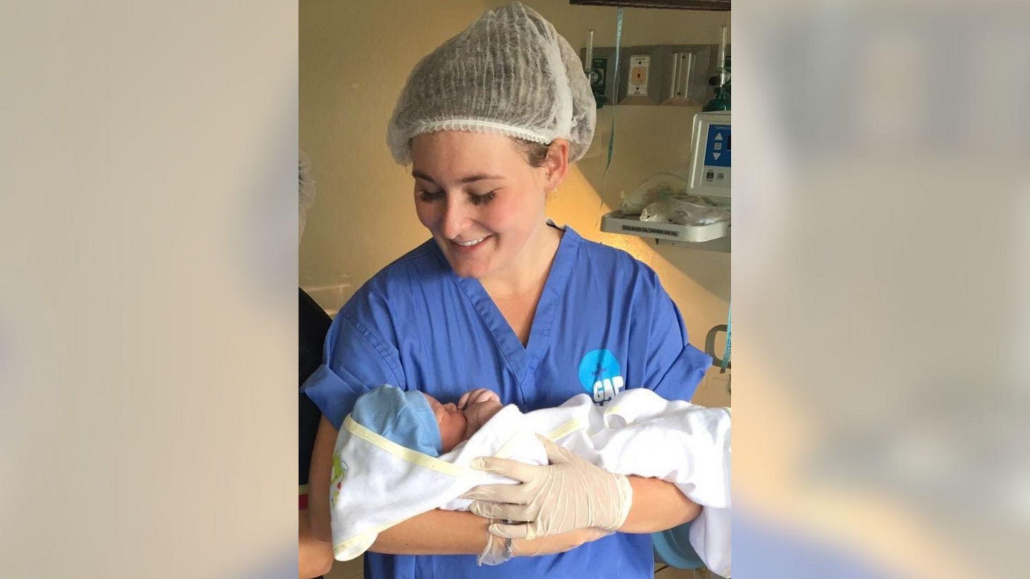 Emily Oliver in blue nurses clothes holding a baby