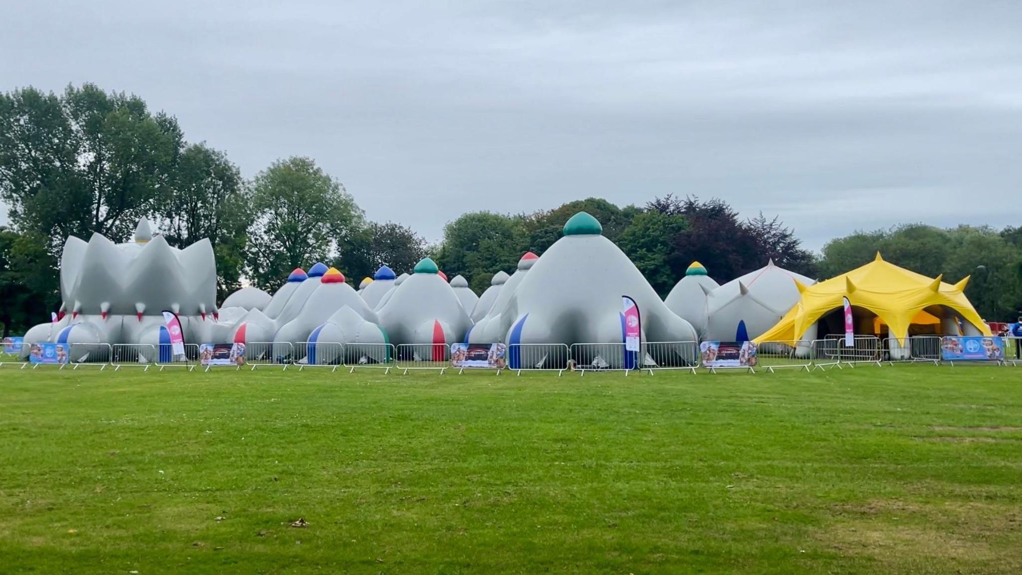 An inflatable grey maze structure stands in a grassy park