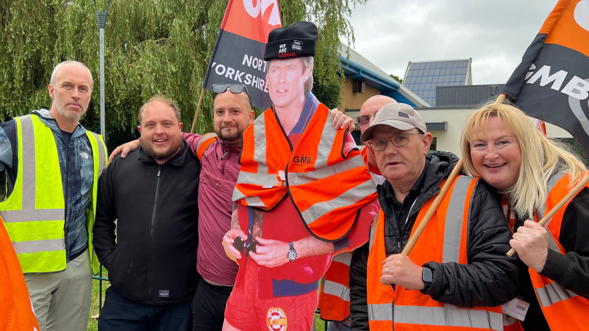 A group of men and women waving GMB flags stand with a cardboard cut-out of Baywatch era David Hasselhoff