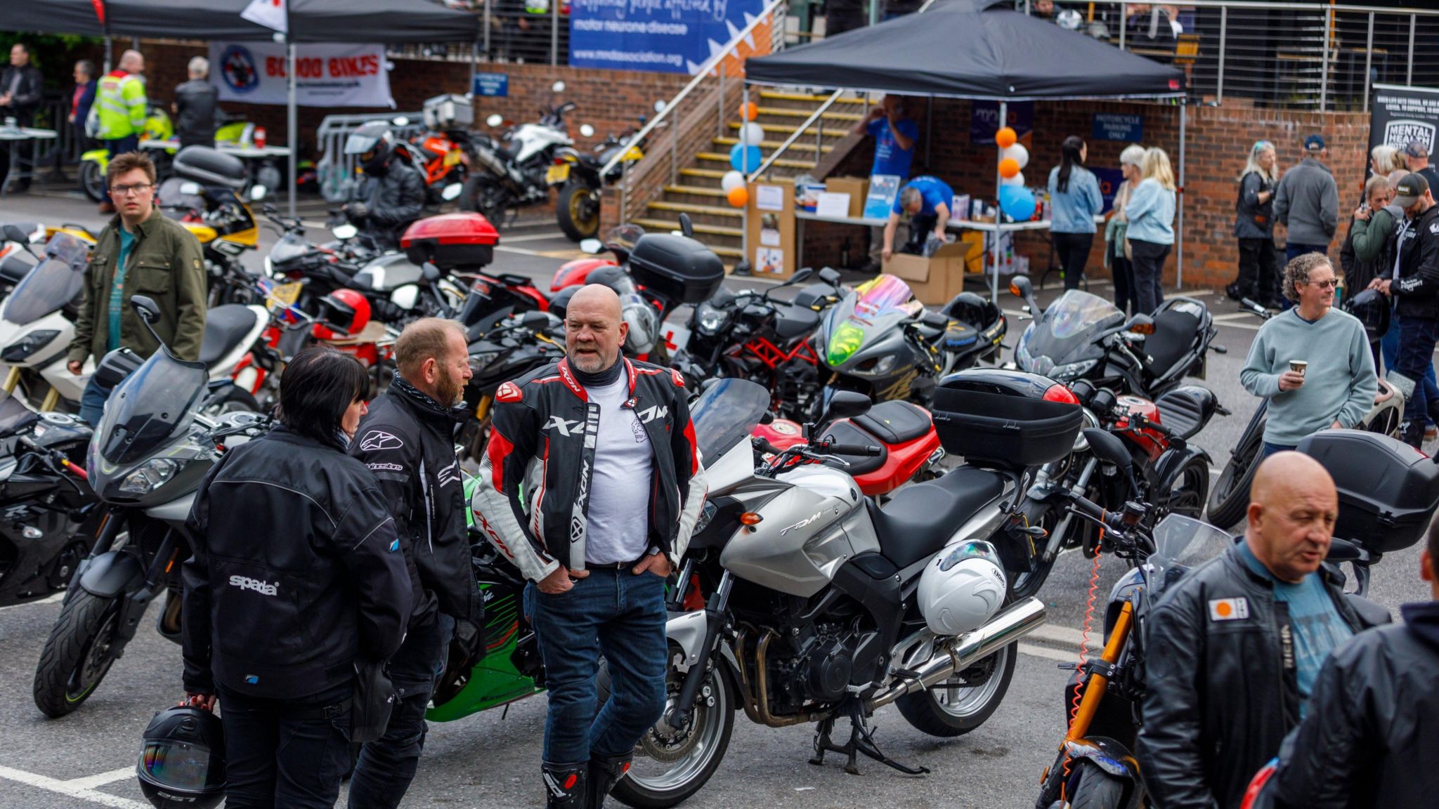People stand in the main car park at Fowlers in Bristol. Many of them are wearing motorbike leathers and there are several motorbikes on display