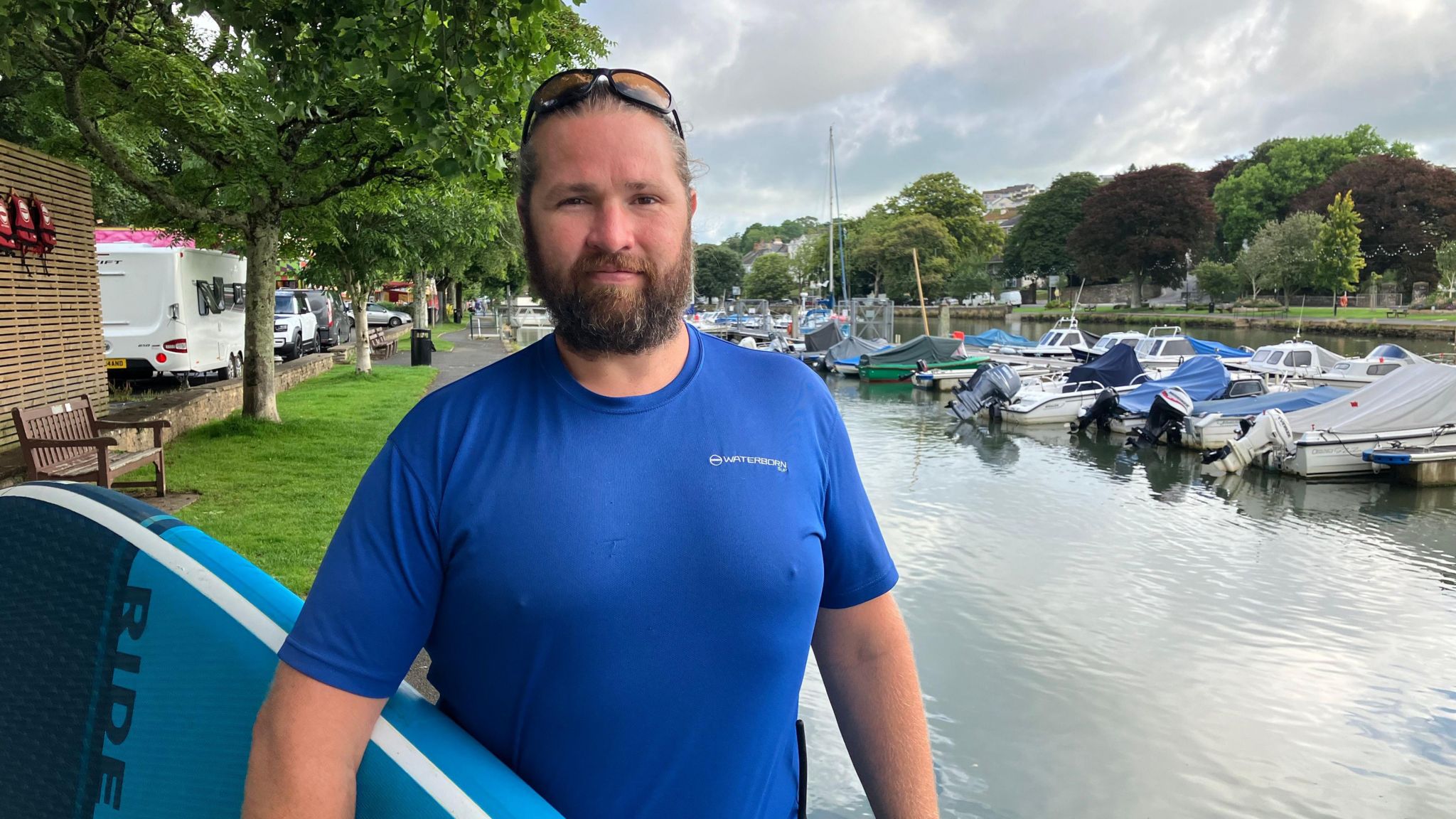 Crispin Jones standing by a river, holding a stand-up paddleboard