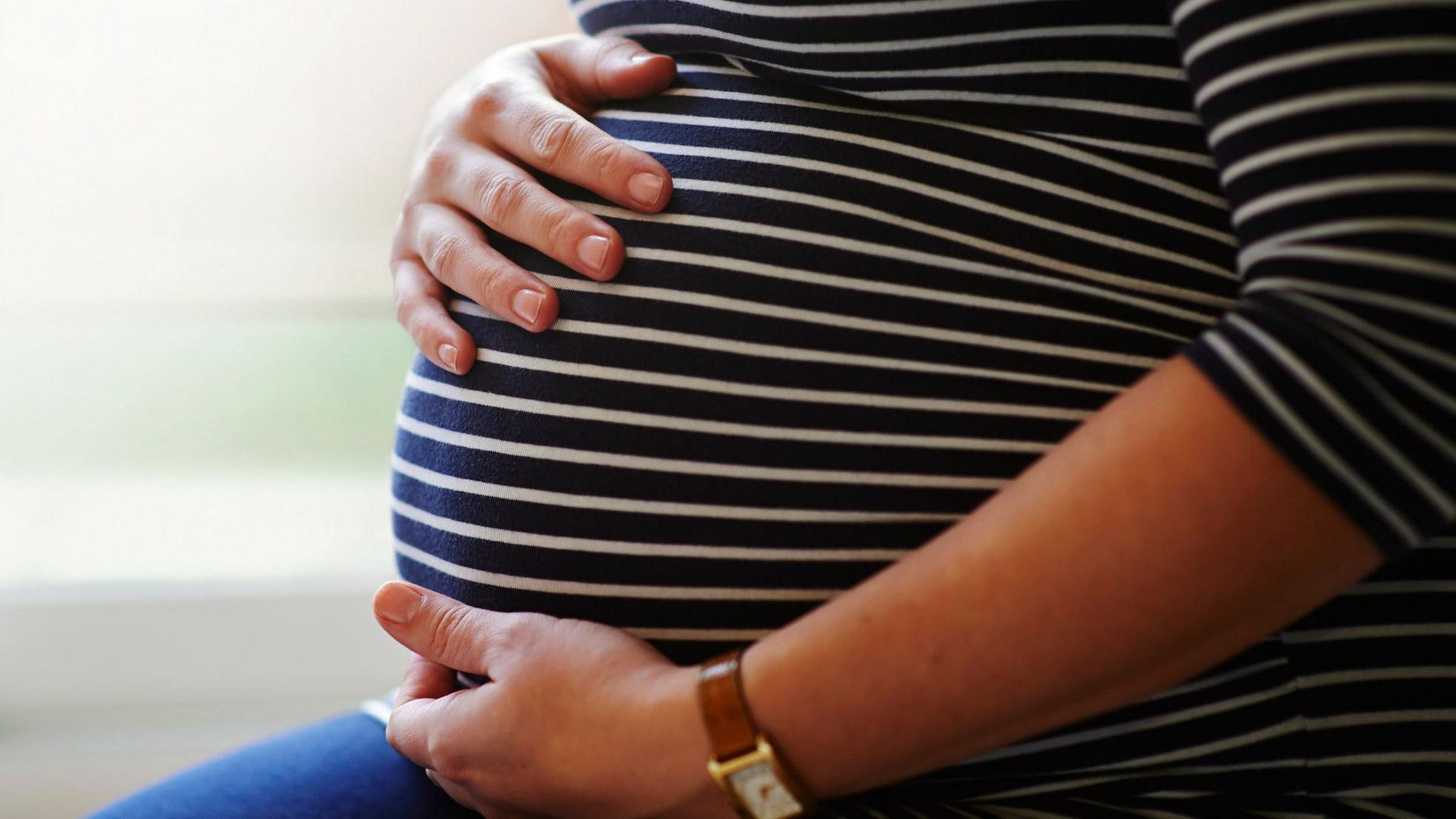 A pregnant woman holds her stomach with a black and white stripped top on