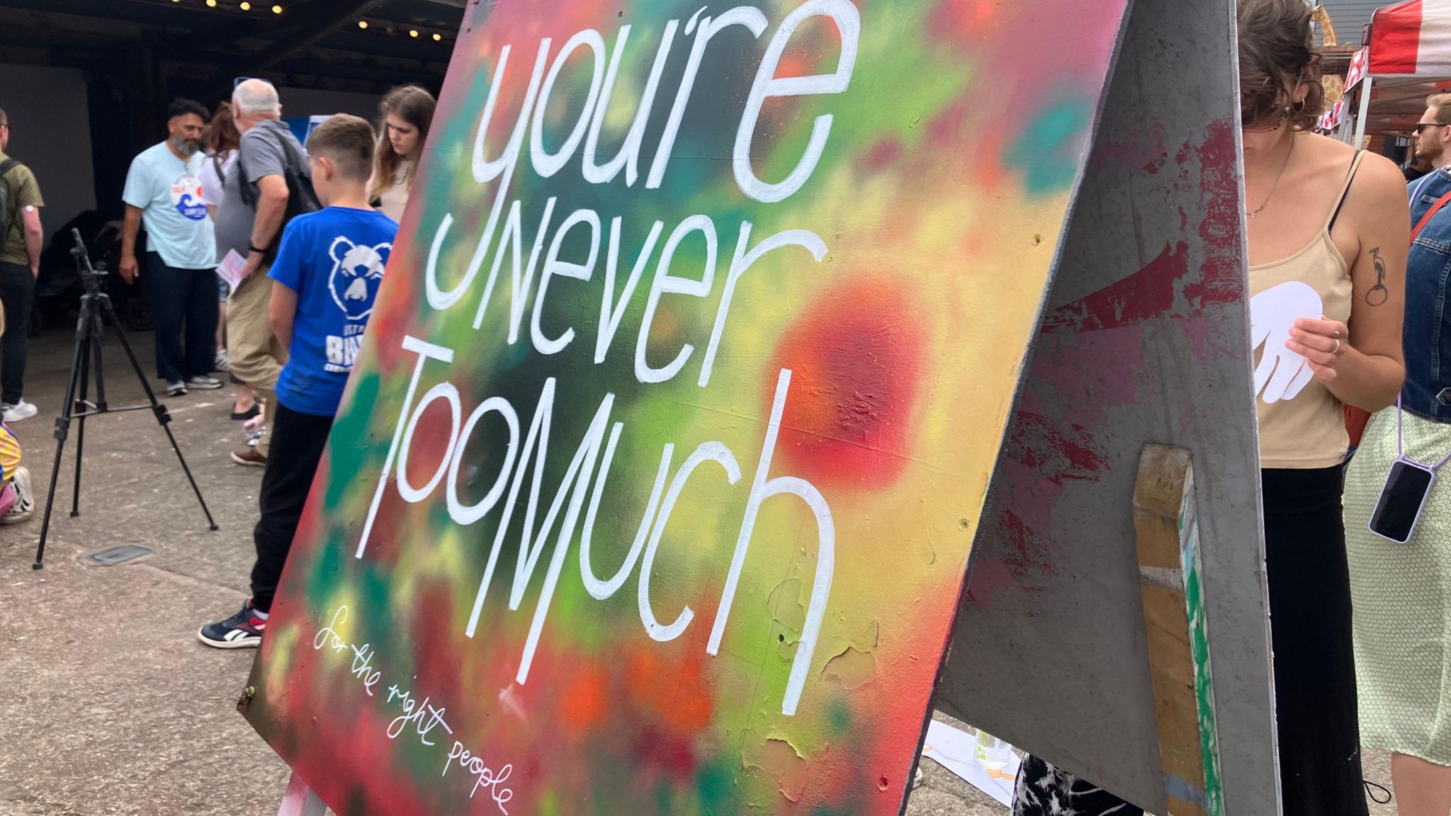 A colourful canvas with the words "you're never too much" painted in white