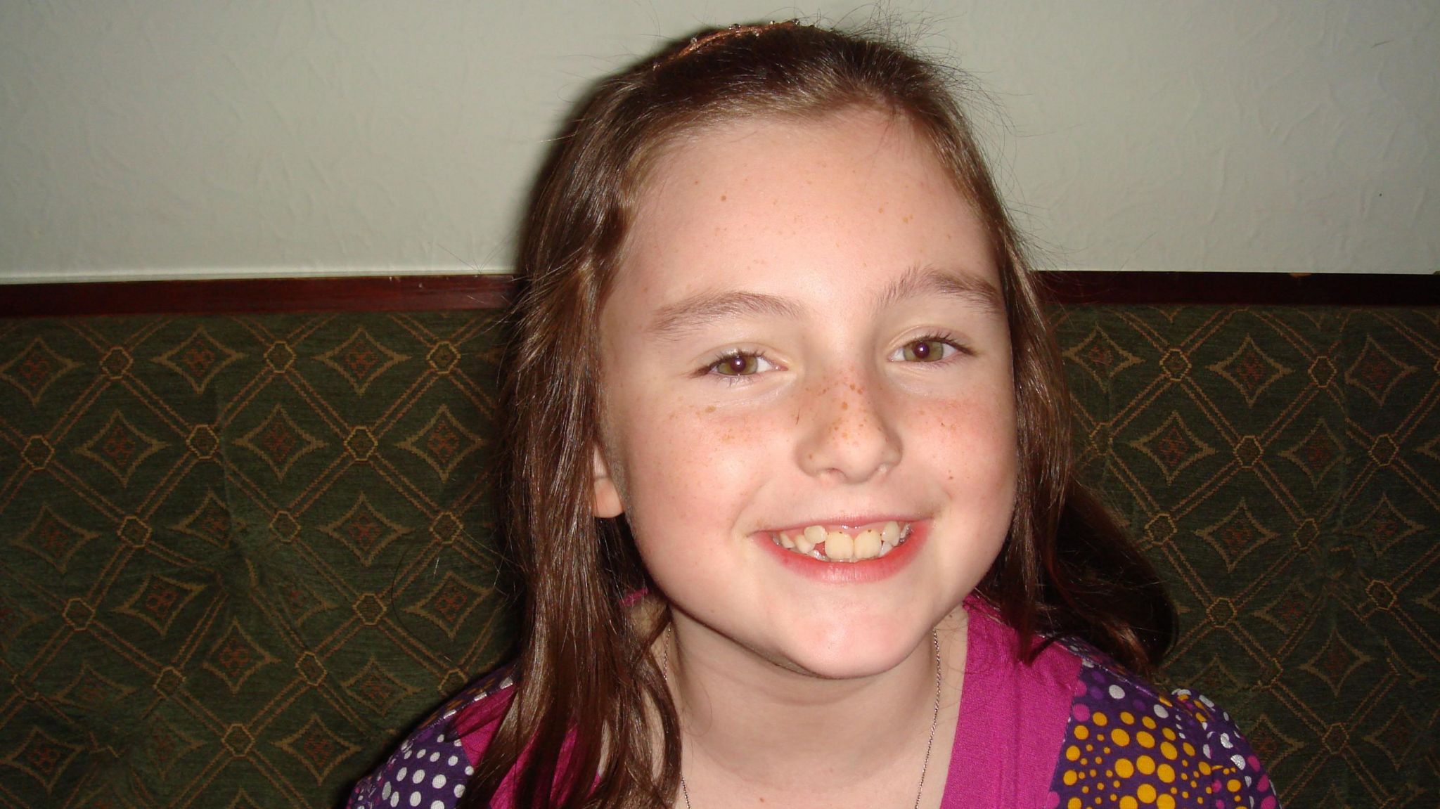 Beth Langton as a child. She is smiling as she looks into the camera and her long brown hair is pulled back from her face by headband 