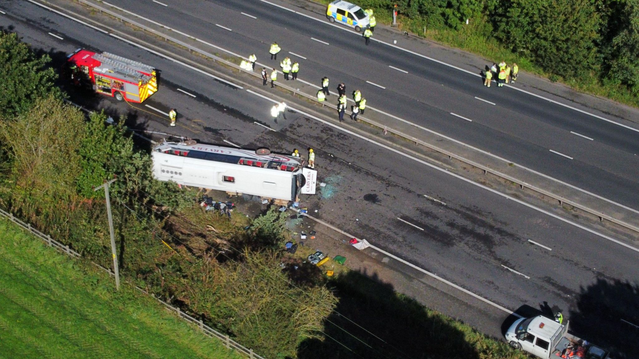 An aerial view of the coach lying on its side with emergency vehicles at the scene