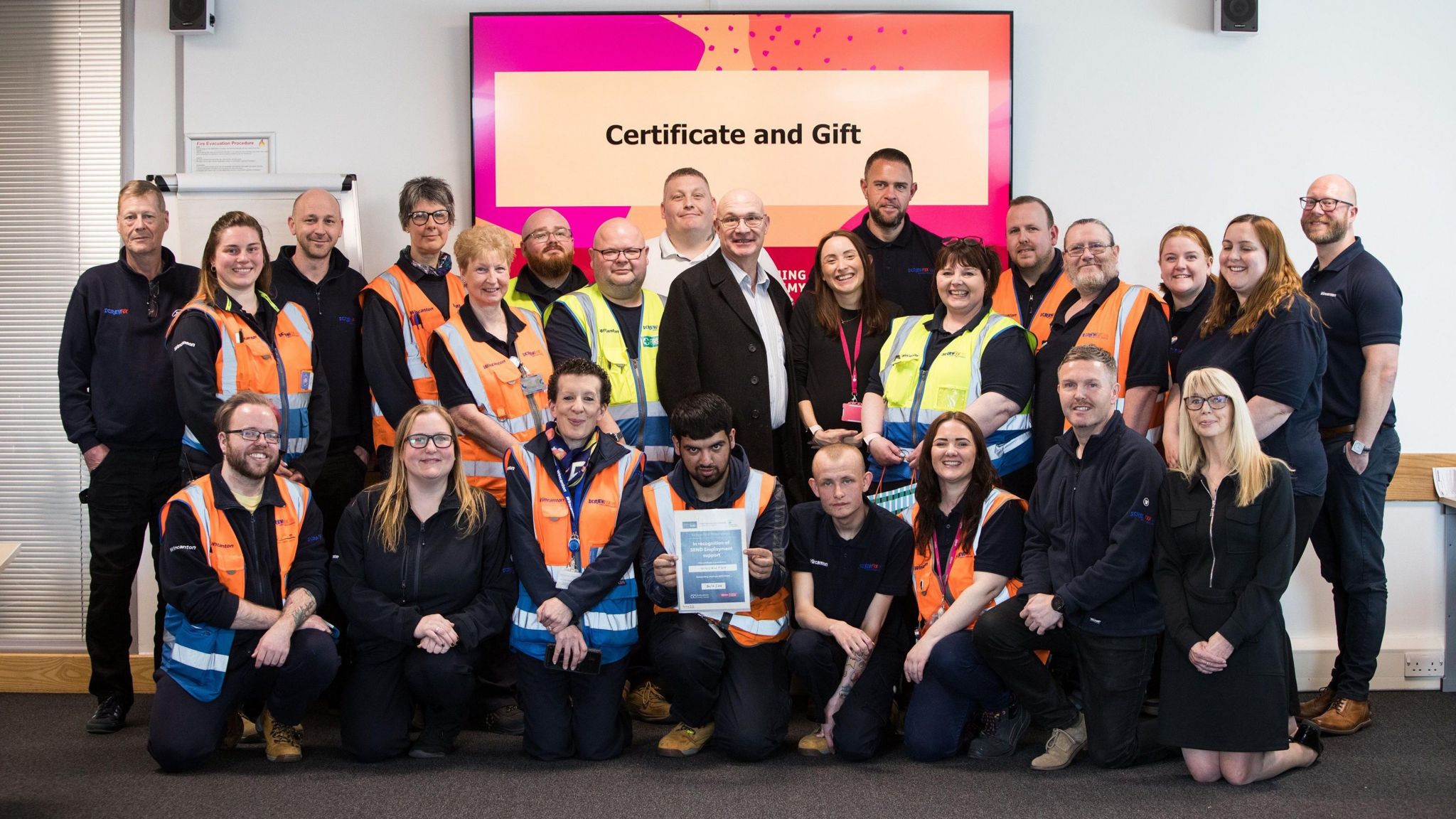 A team of twenty five employees are presented with a certificate.