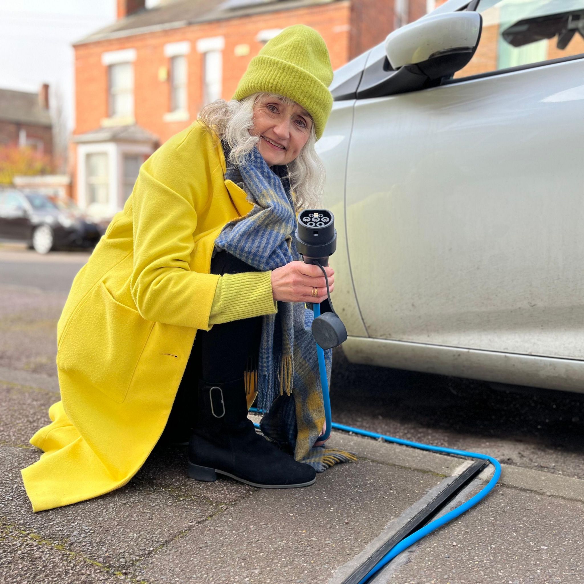 A woman crouching down next to a car holding an electric charger
