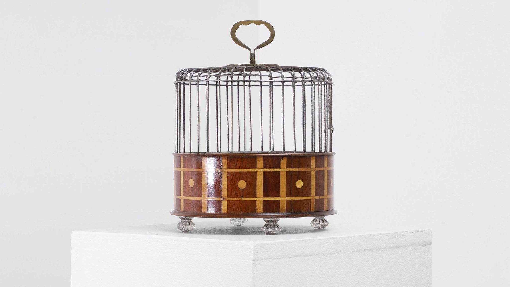 A wooden birdcage placed on top of a white table. The birdcage is brown and has a round handle on top.