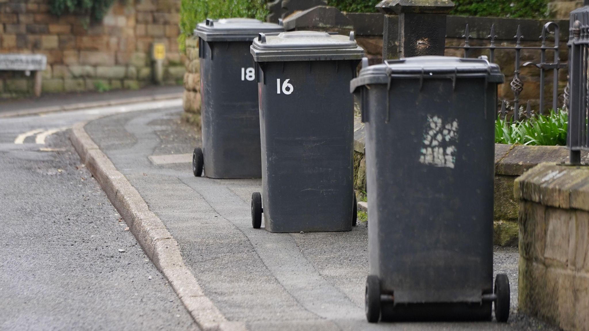 Three black wheelie bins along a road.