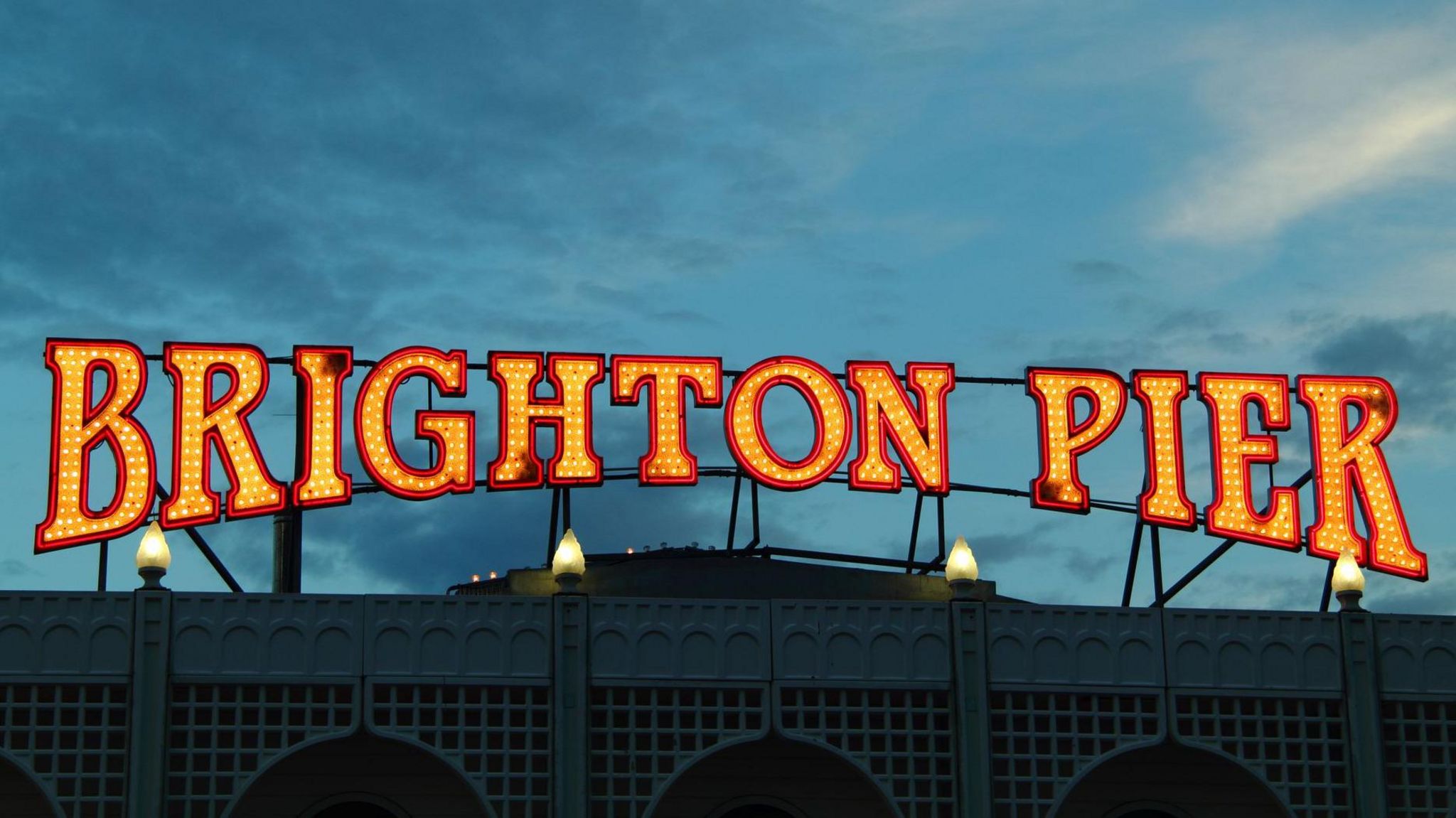 A bright neon sign reads Brighton Pier against a dark sky. 