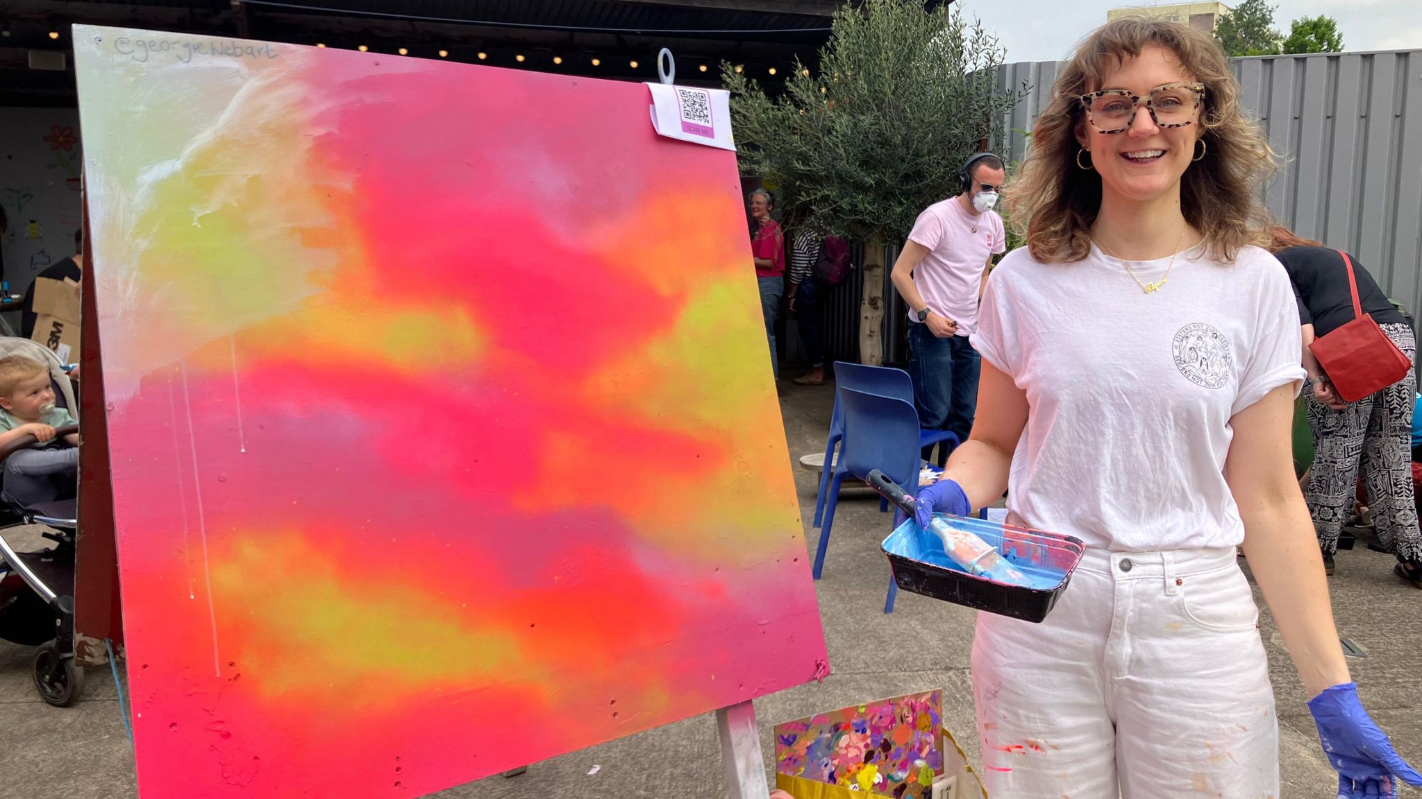 Georgie Webb standing next to a canvas with orange pink and yellow tones