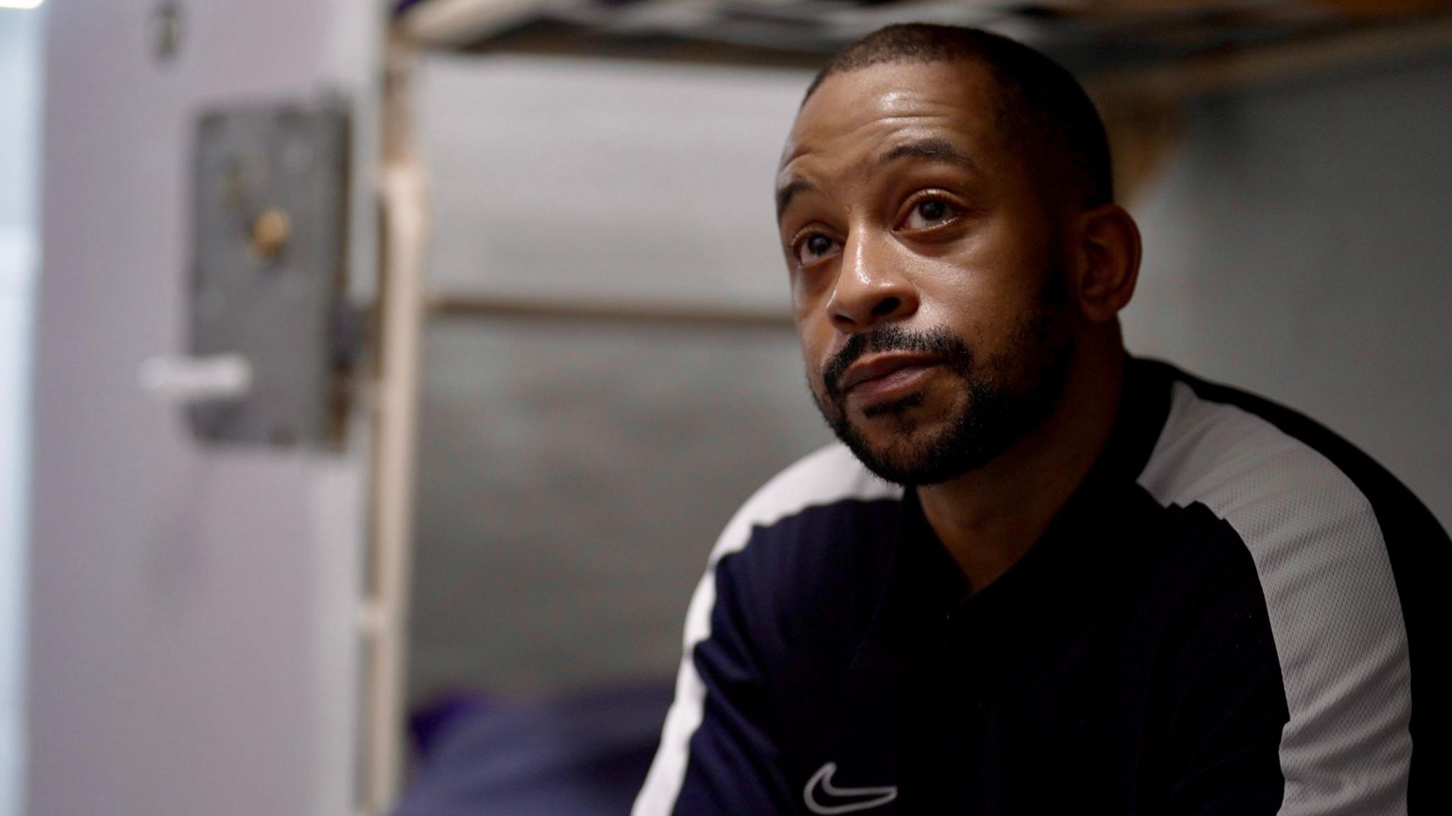 Michael Lewis, dressed in a blue Nike sweatshirt with white sleeves, sits on a bunk in a cell at Pentonville prison, north London.