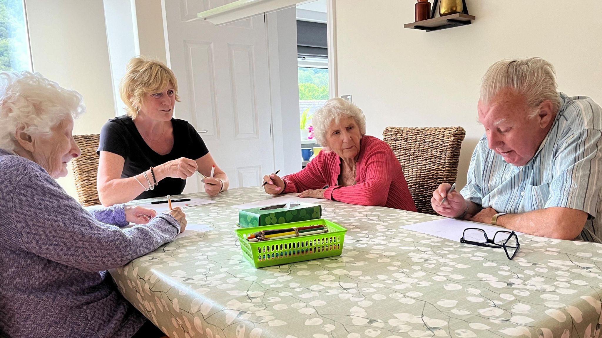 Three elderly people sitting around a table writing with a female host