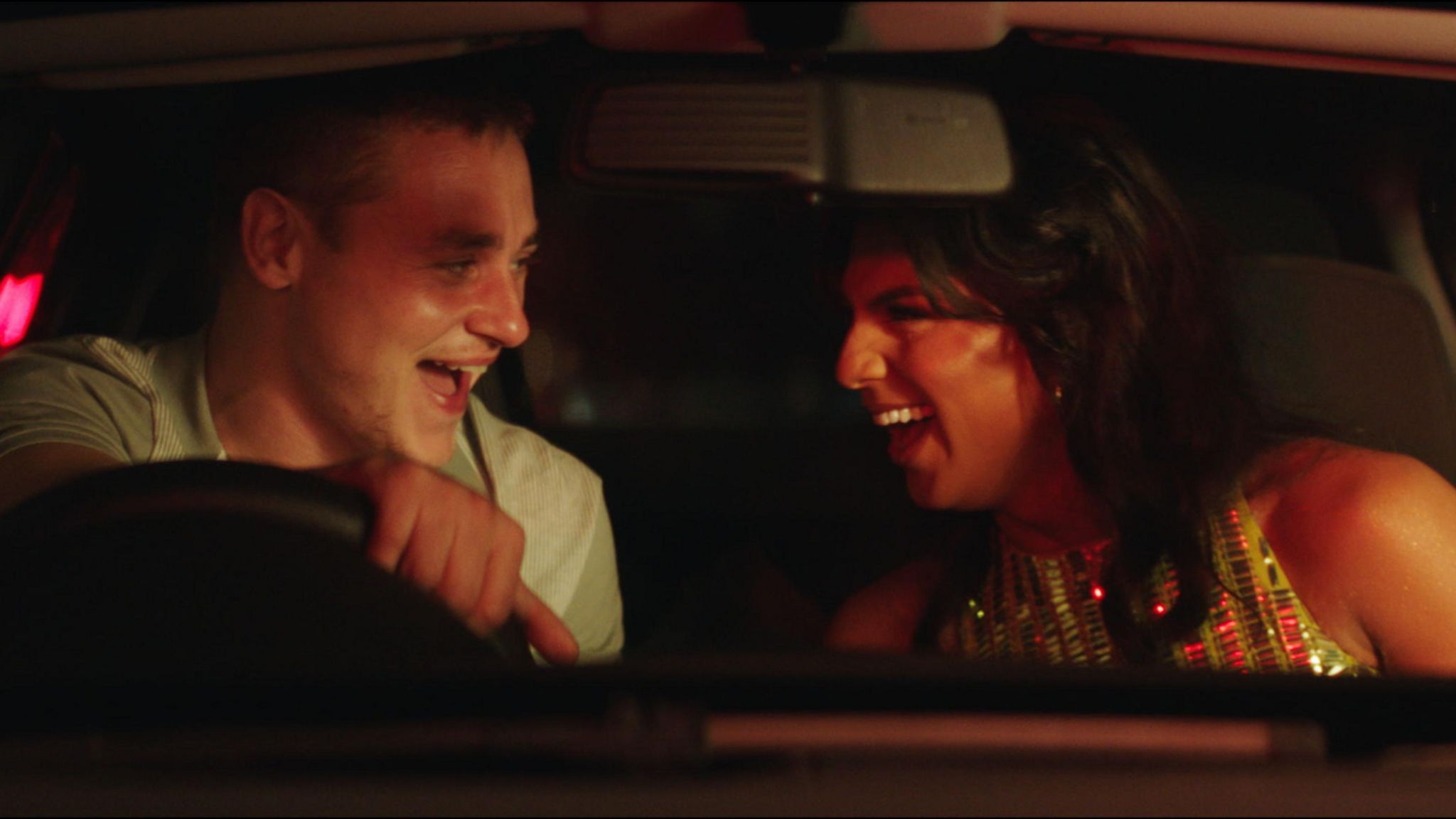 Luke (played by Ben Hardy) and Aysha (played by Jason Patel) laughing together in a car