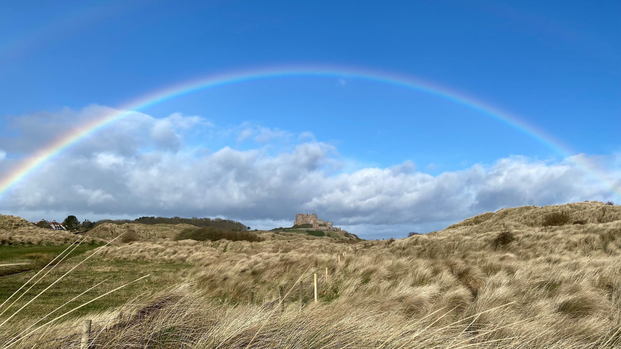 Mainly blue sky with a double rainbow and shower clouds in the distance over Bamburgh Castle