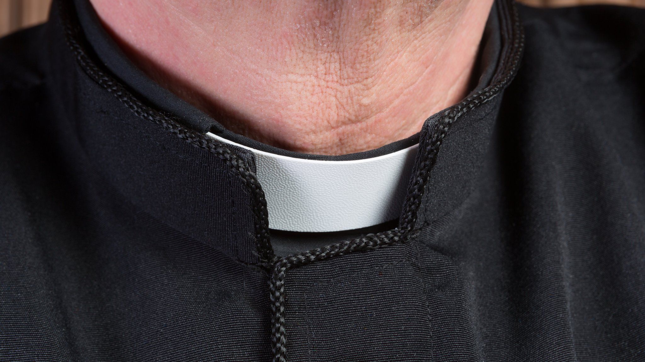 Image shows close-up of the neck of a priest wearing a black shirt with cassock and white clerical collar