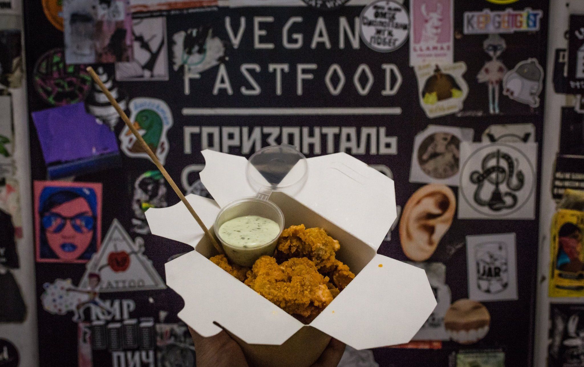 A box of tofu-seitan nuggets being held up in front of the sign for Horizontal
