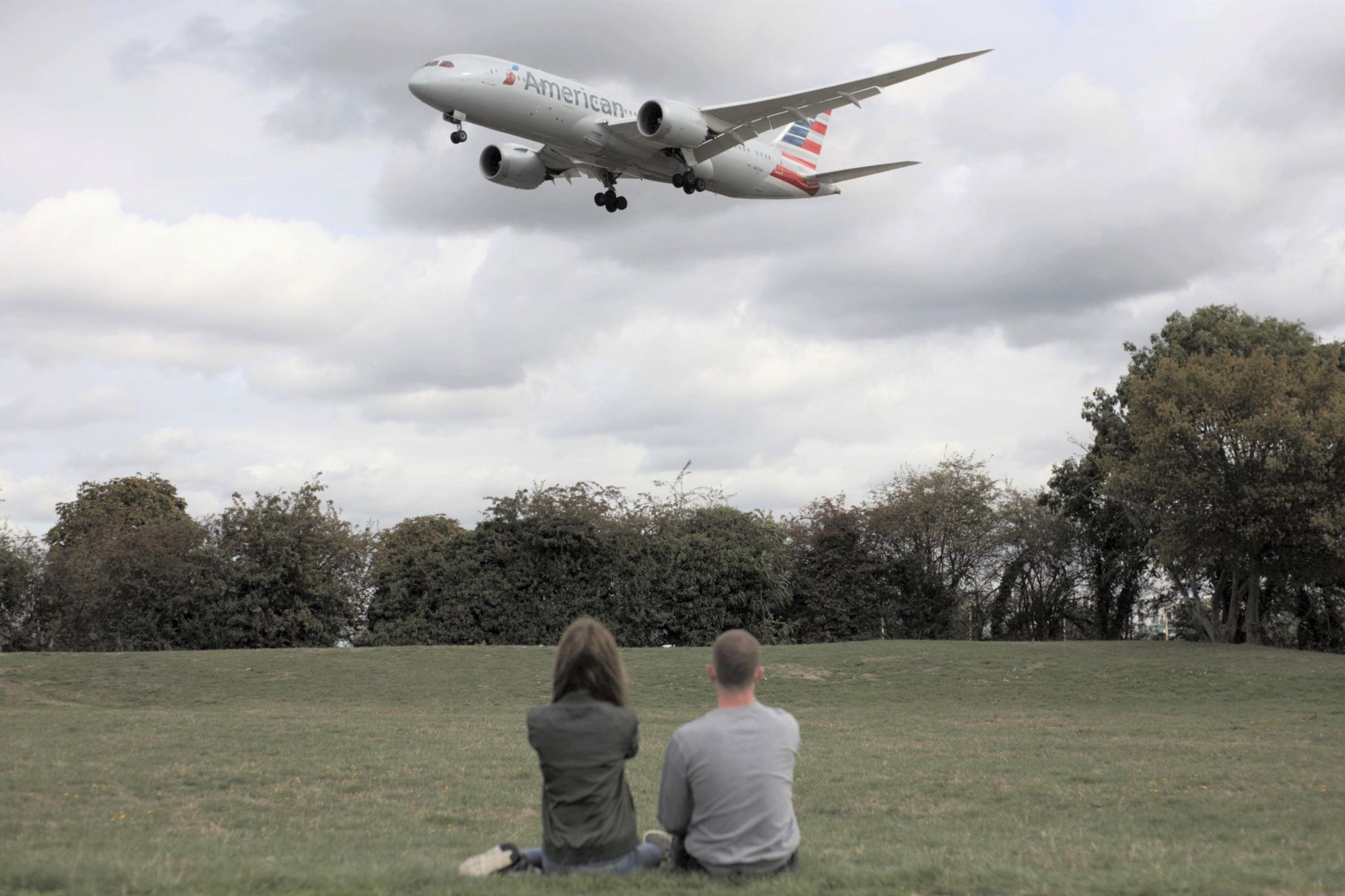 Two people in a park watch American Airlines flight land