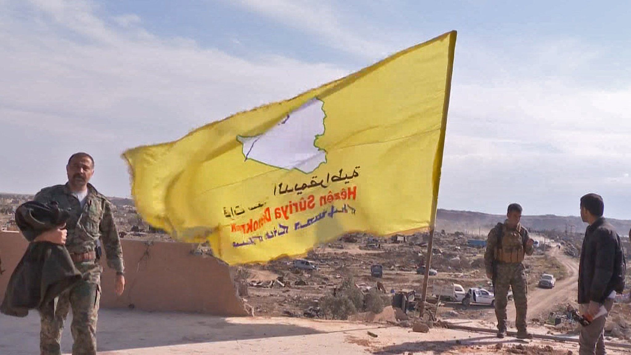 Syrian fighters raise a yellow flag as they celebrate the defeat of IS