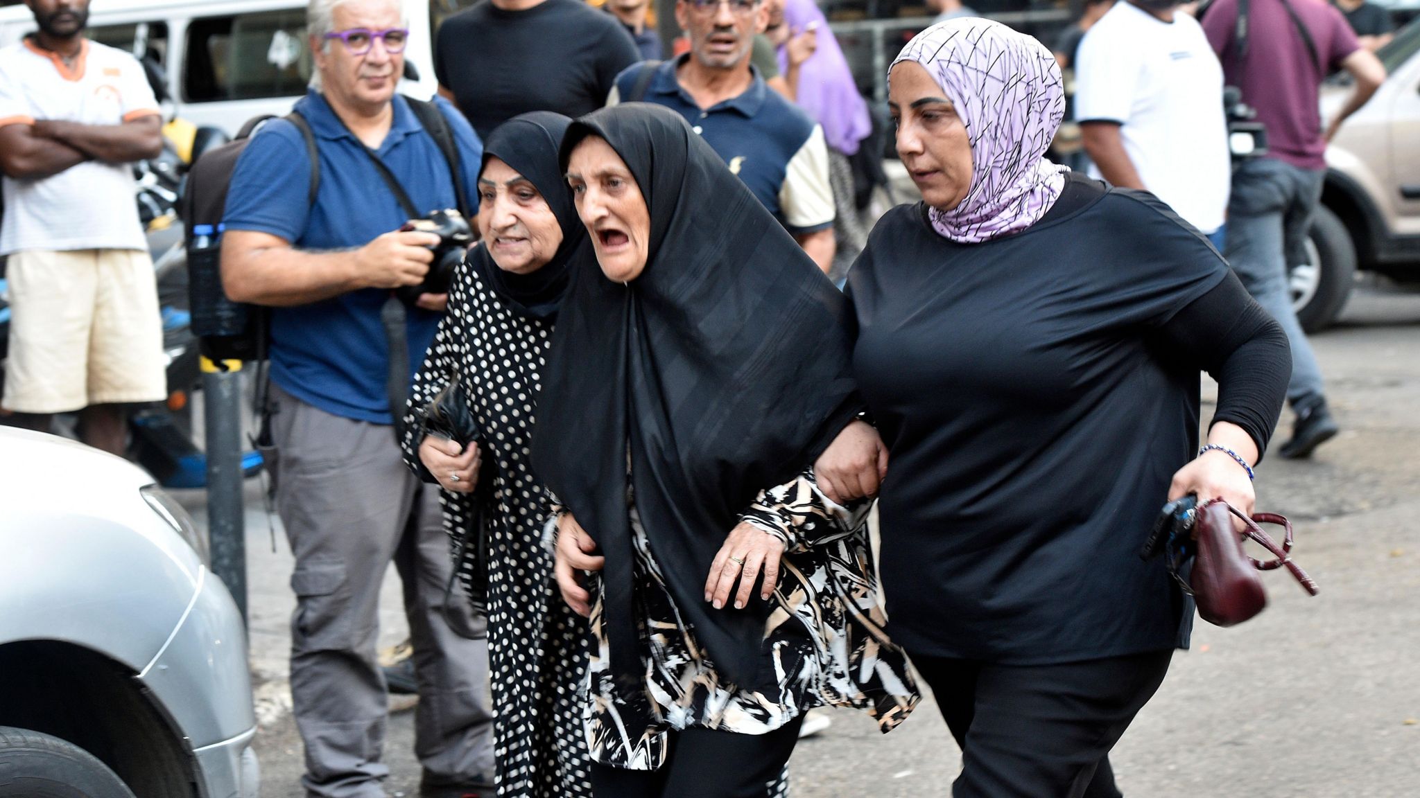 Three women link arms as they walk towards a hospital