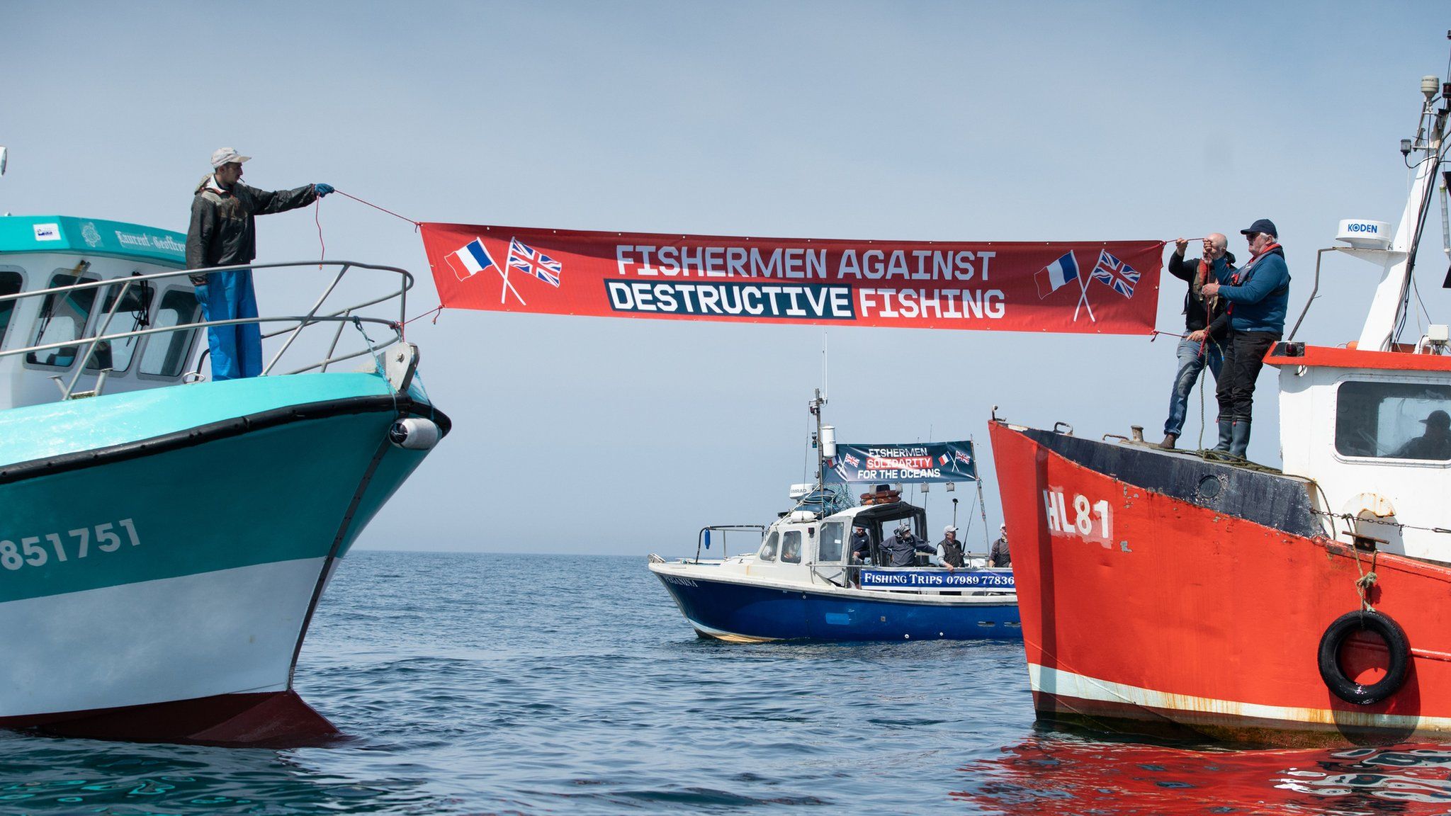 A banner being held between two boats in the Channel