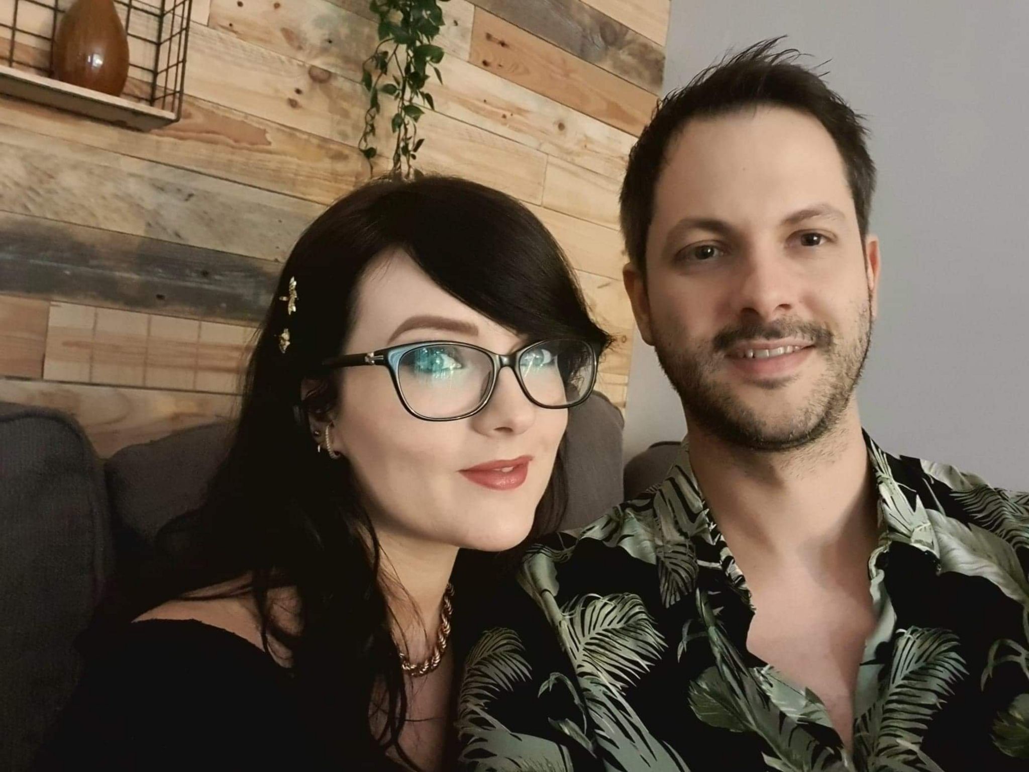 A lady with long dark hair and glasses next to a man with dark hair and stubble.