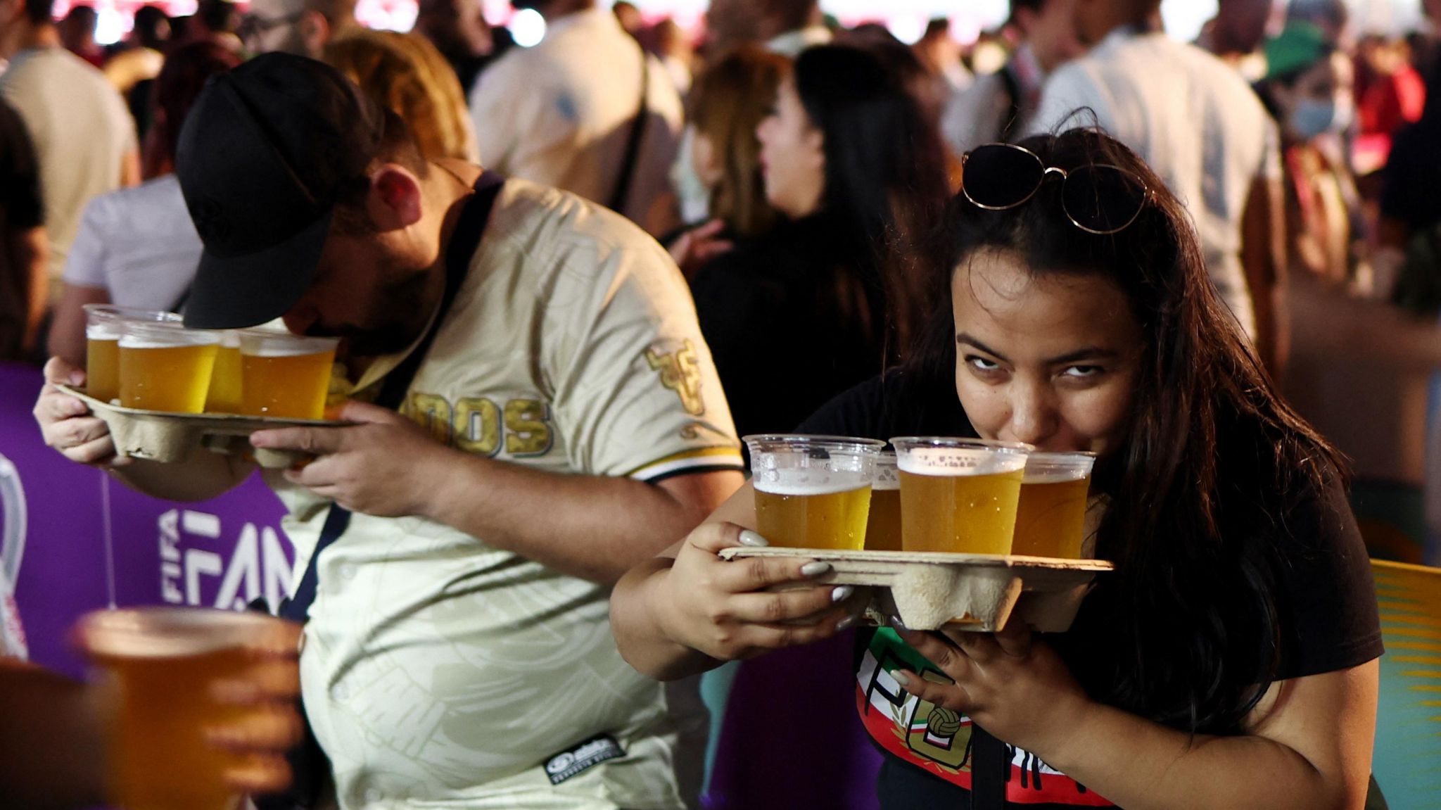 A woman holding four plastic cups of beer and sipping from one