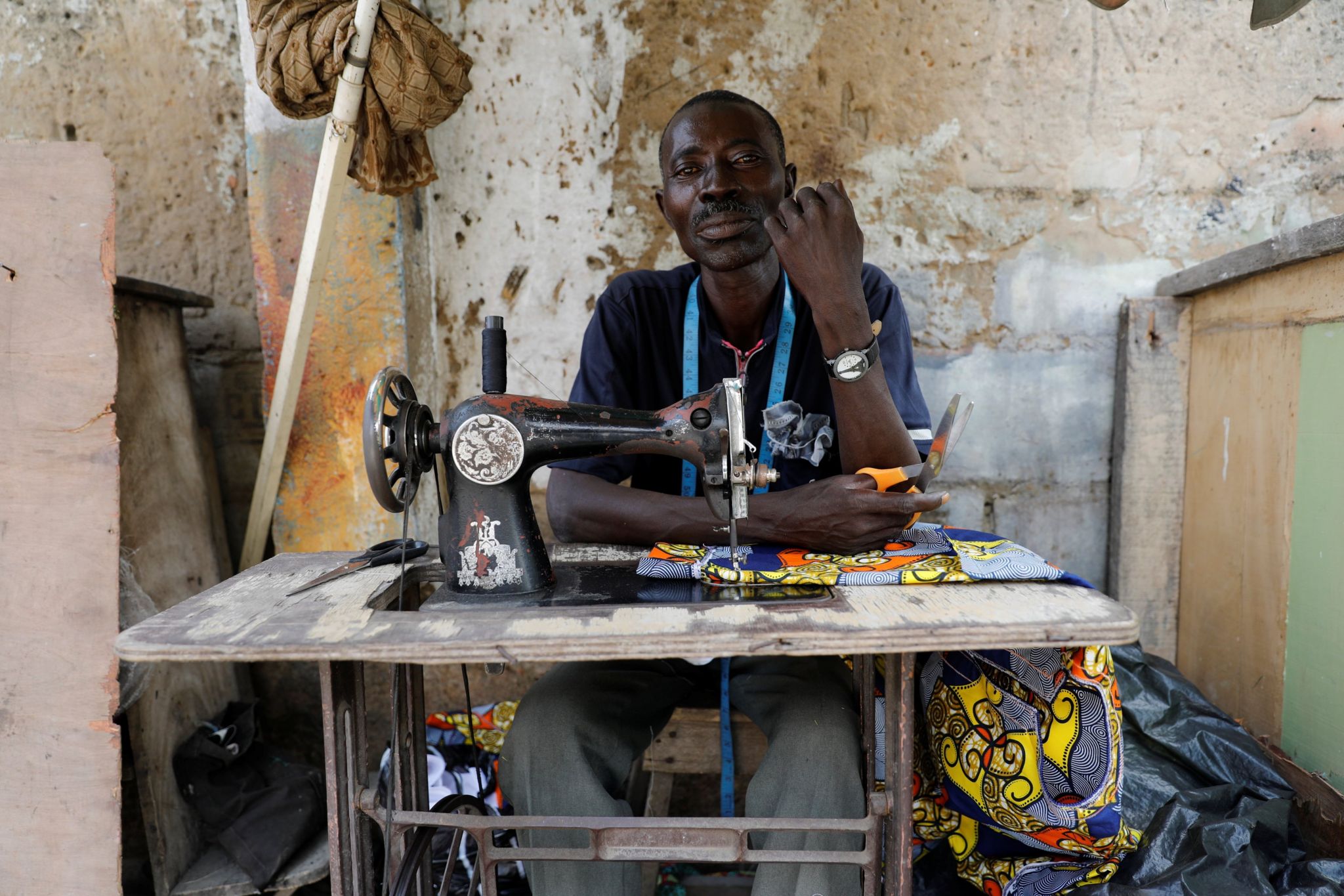 Streetside tailor Ganiyu Oyinlola sits behind a sewing machine for a portrait photograph as he sews near a currency exchange market in Ikeja district in Lagos, Nigeria August 12, 2017.