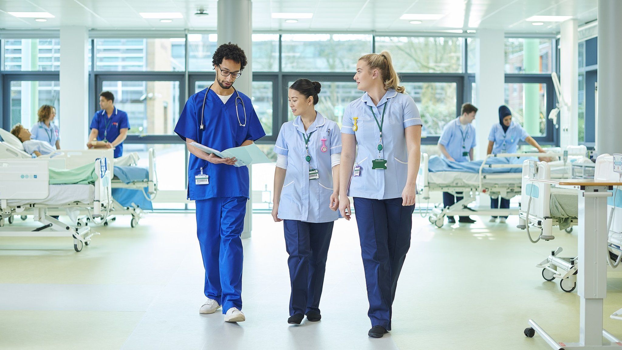 Three nurses walk along a ward