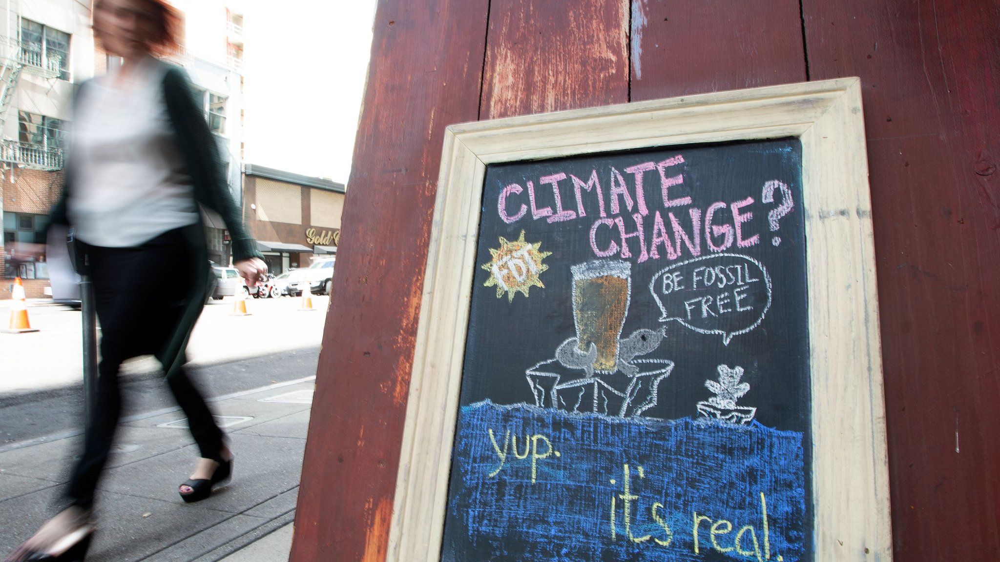 A woman walks by a sign about climate change in front of a bar in downtown San Francisco. September 2018