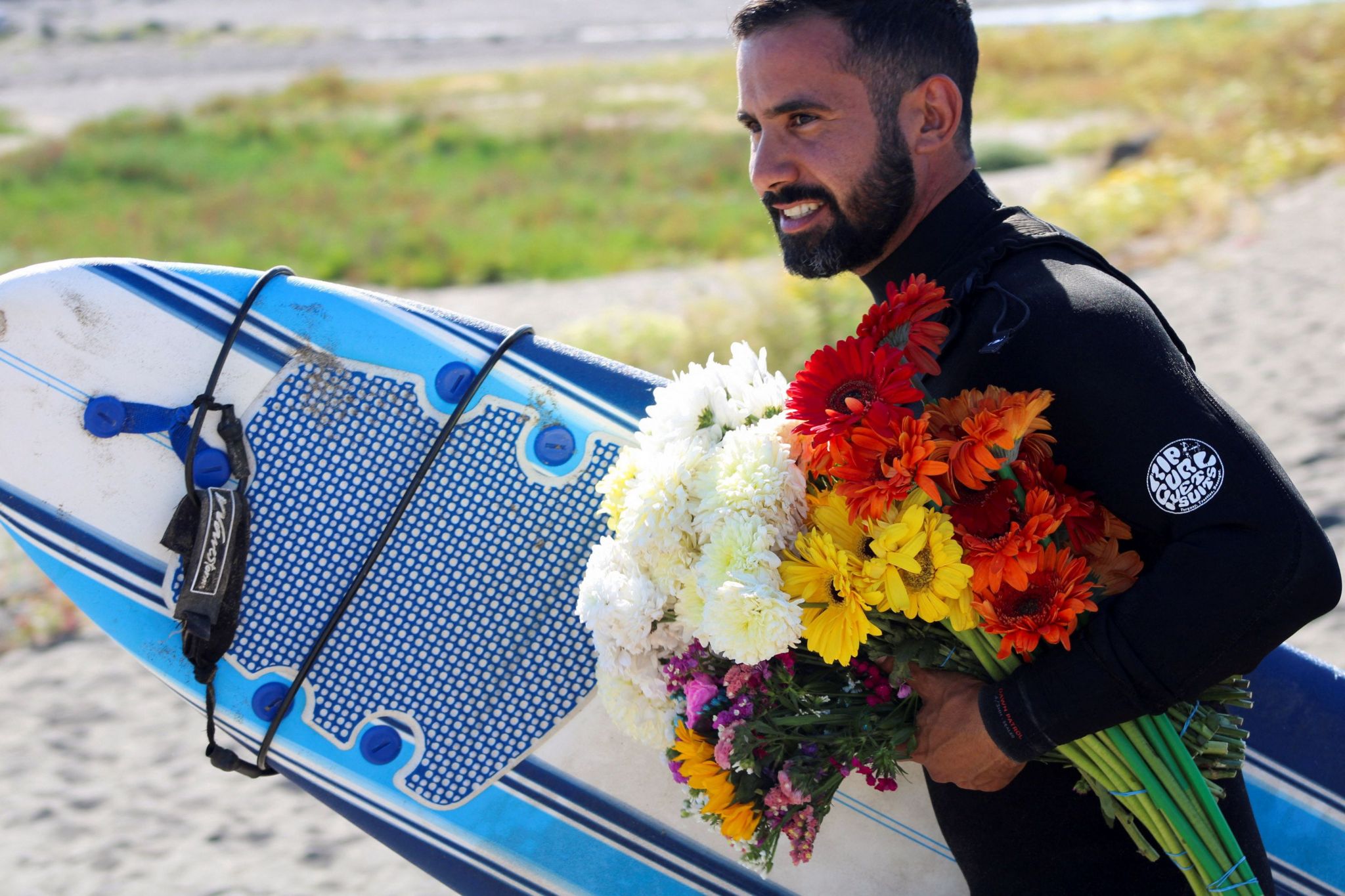 A surfer carries flowers with a surf board