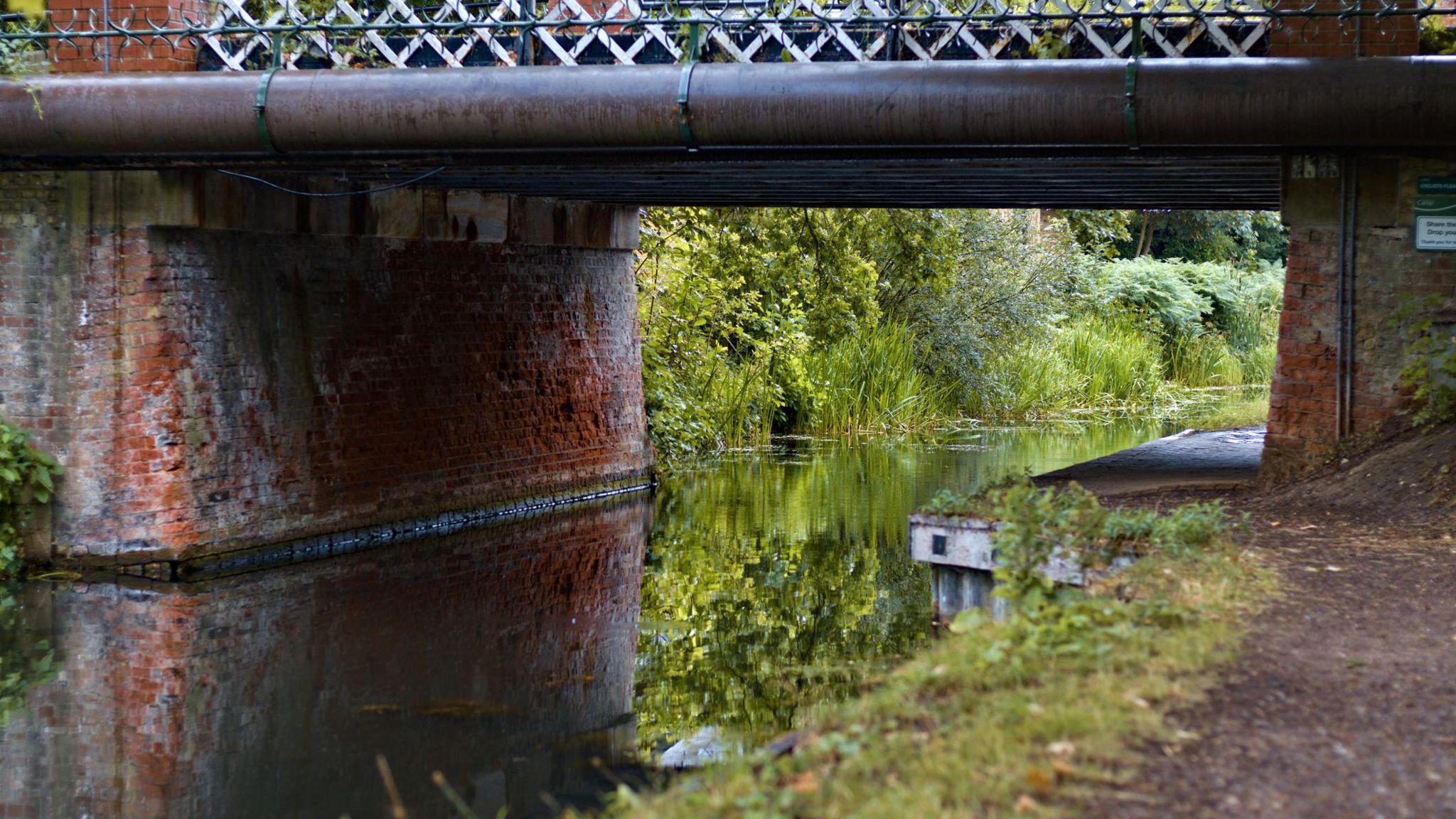 A close up of an old brick built bridge over a canal, with greenery in the distance and the towpath to the right