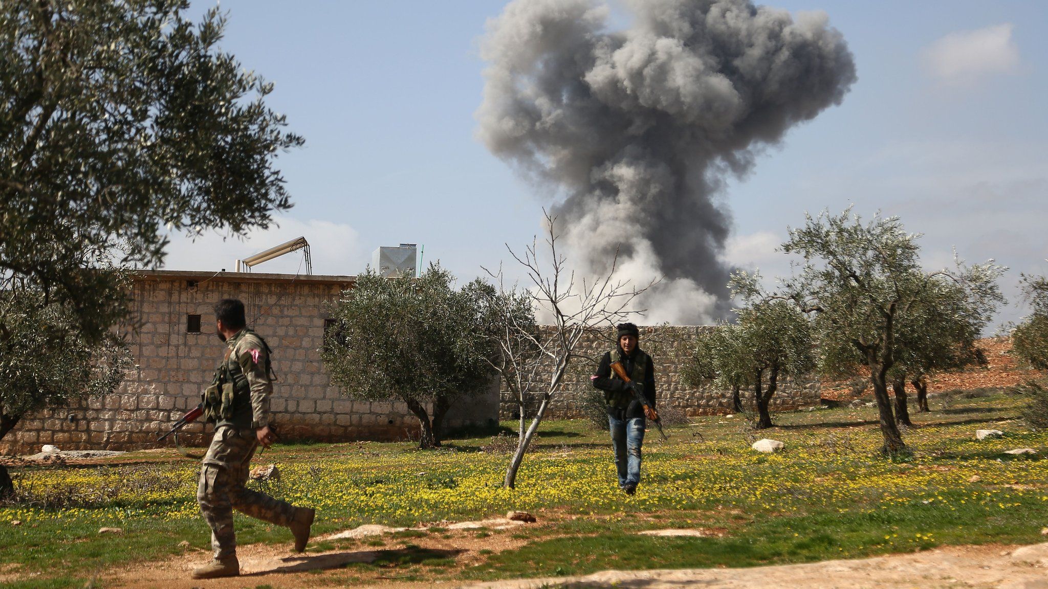 Turkish-backed Syrian opposition fighters are seen in the village of Jamanli, northeast of the Syrian city of Afrin, on March 3, 2018, as smoke billows in the background from a reported Kurdish People's Protection Units (YPG) location.