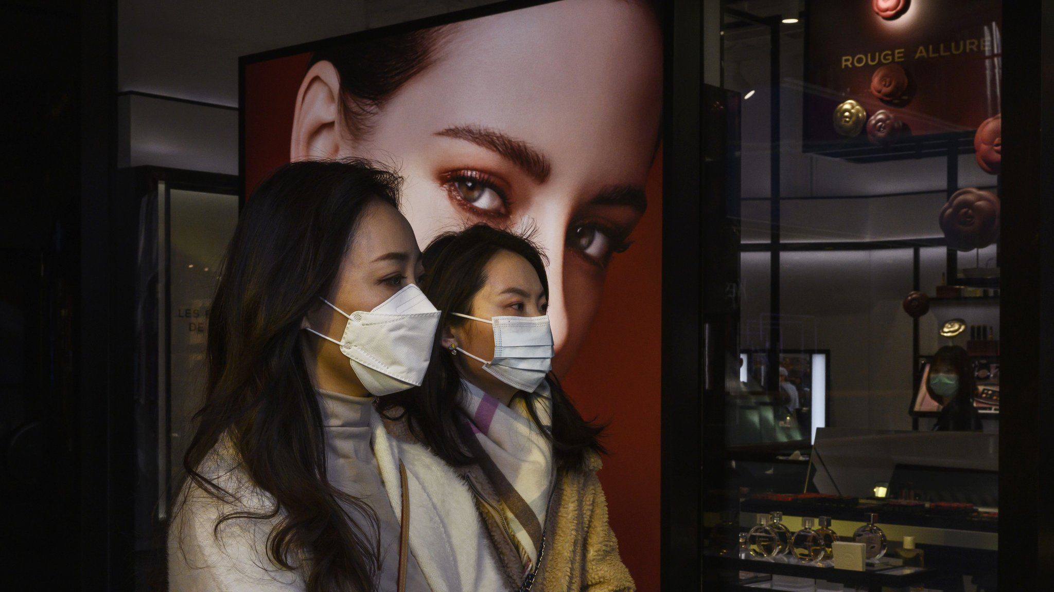 Chinese women wear protective masks as they walk by a luxury store while shopping in Sanlitun on March 10, 2020 in Beijing, China.