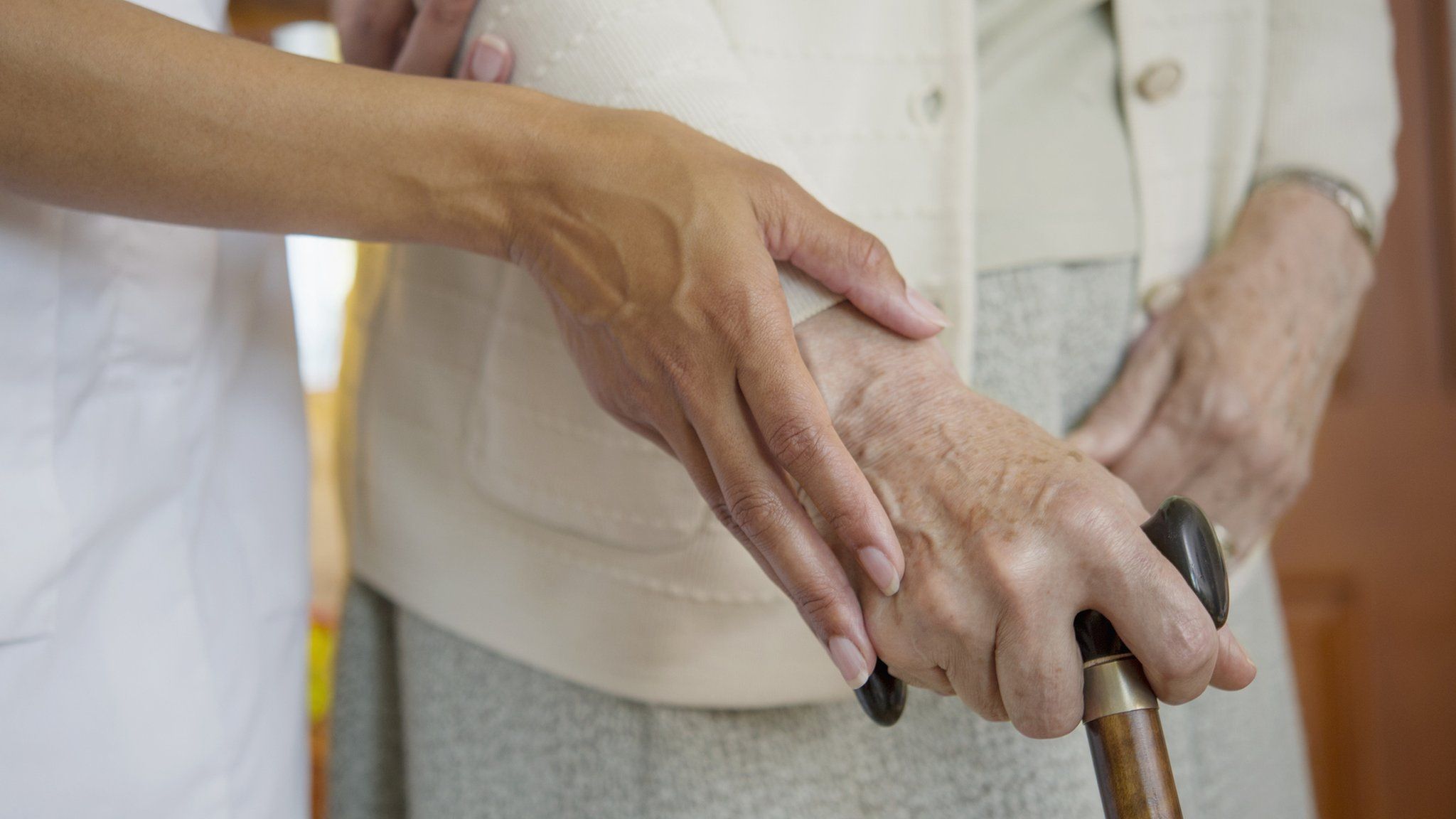 A carer guiding an elderly person with a walking stick