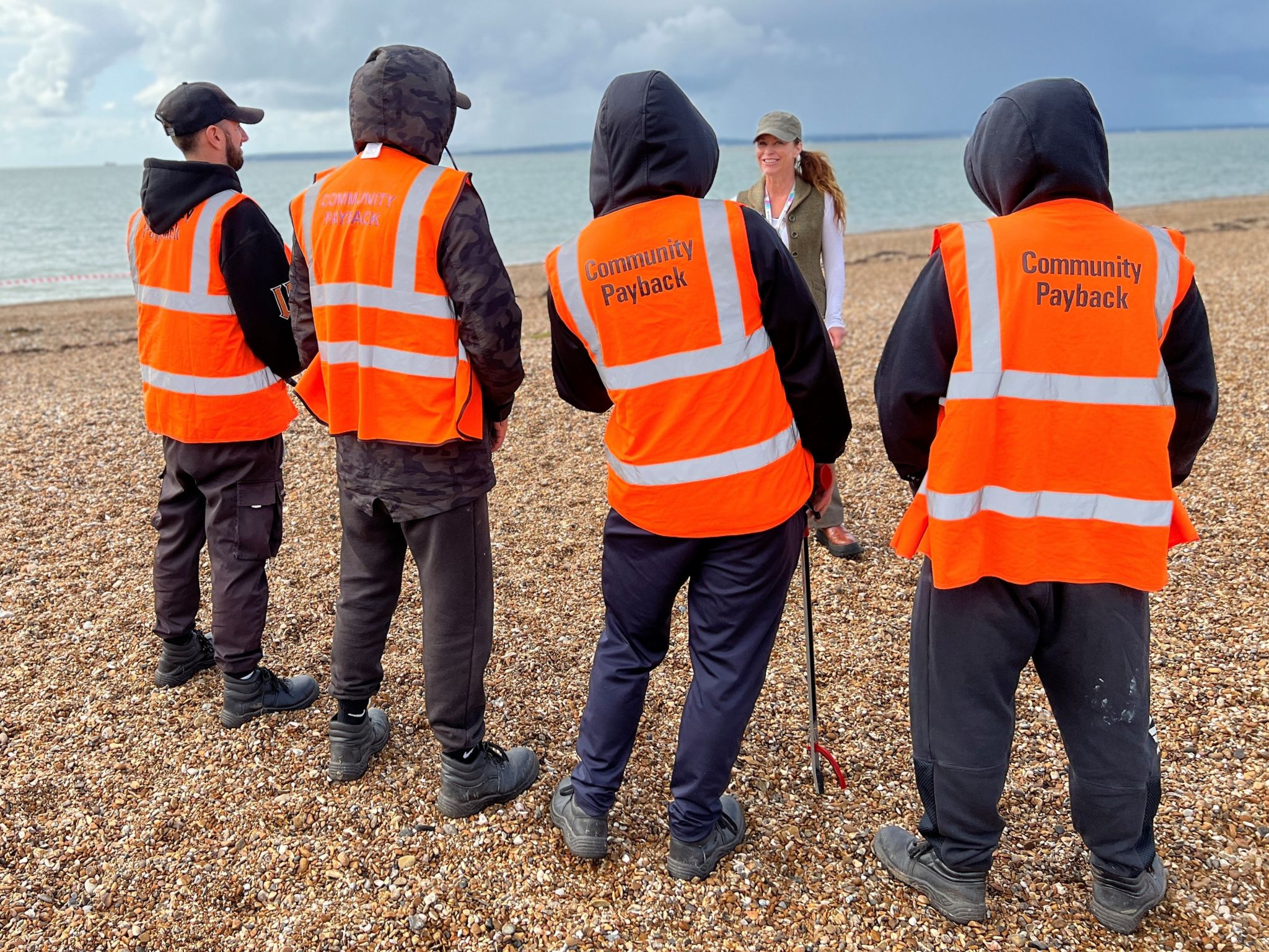 Offenders in fluorescent orange jackets standing on a beach