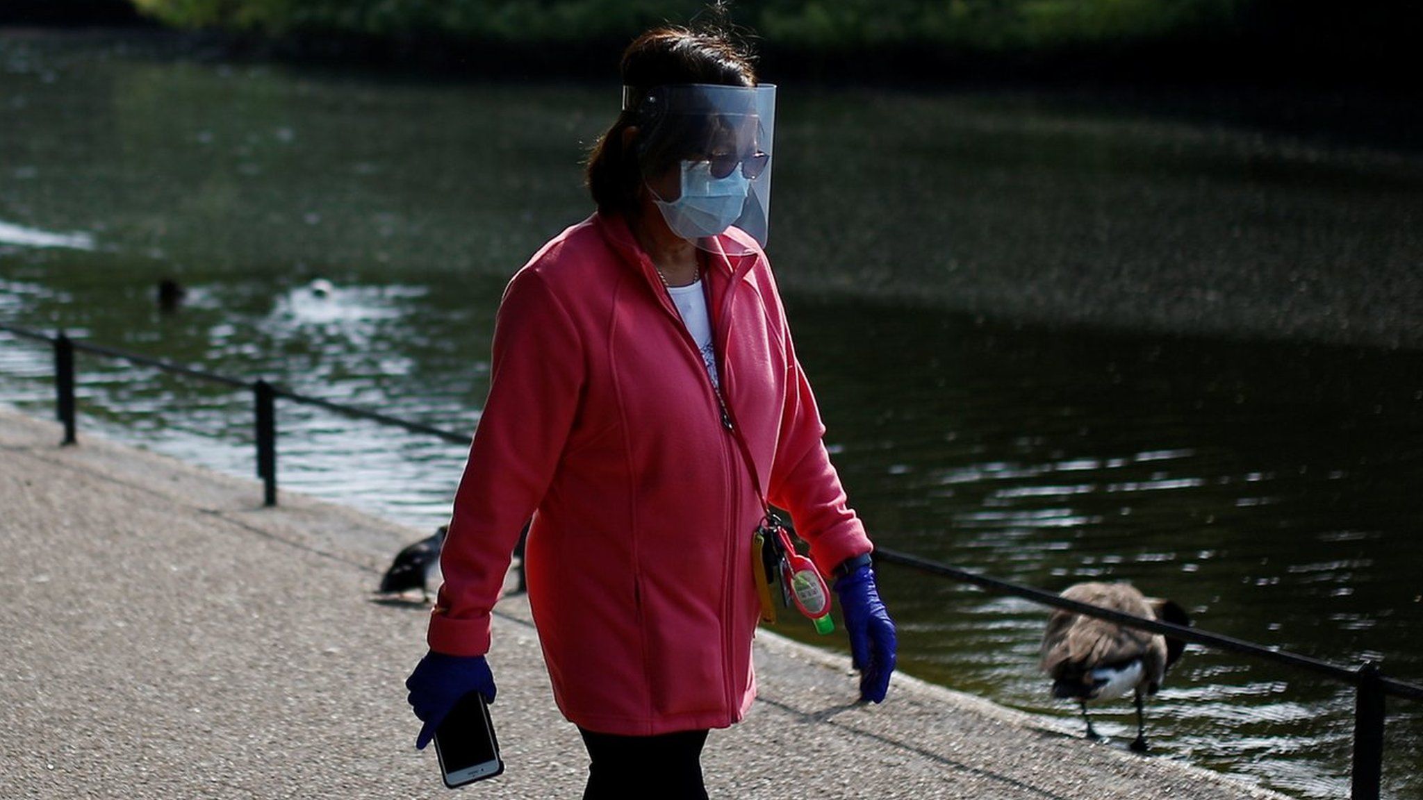 A woman wearing a protective face mask and visor walks in St James"s Park