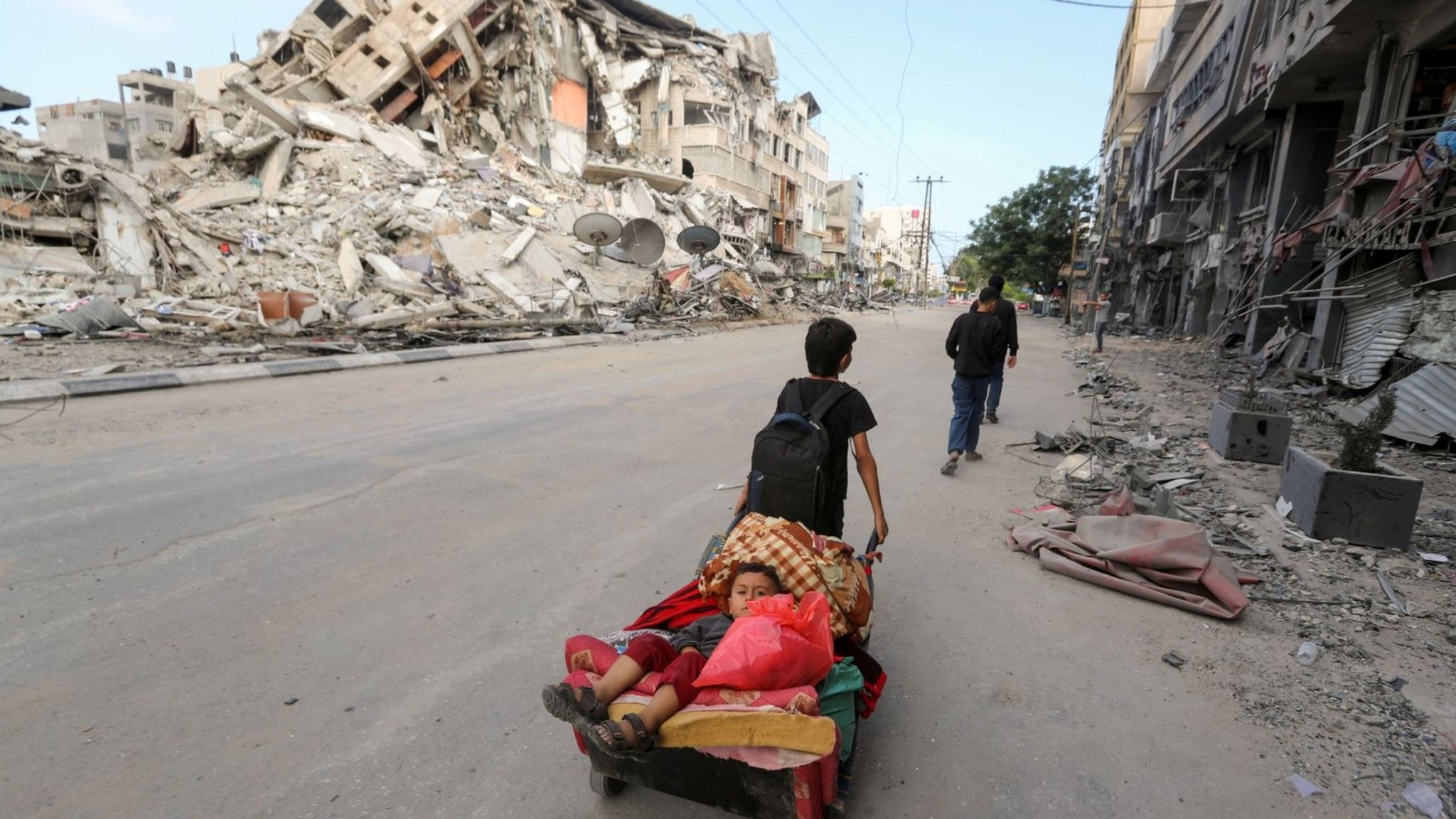 A Palestinian boy pulls a cart carrying his brother and their belongings as they flee their home during Israeli air and artillery strikes, near the site of destroyed a tower block in Gaza City (14 May 2021)