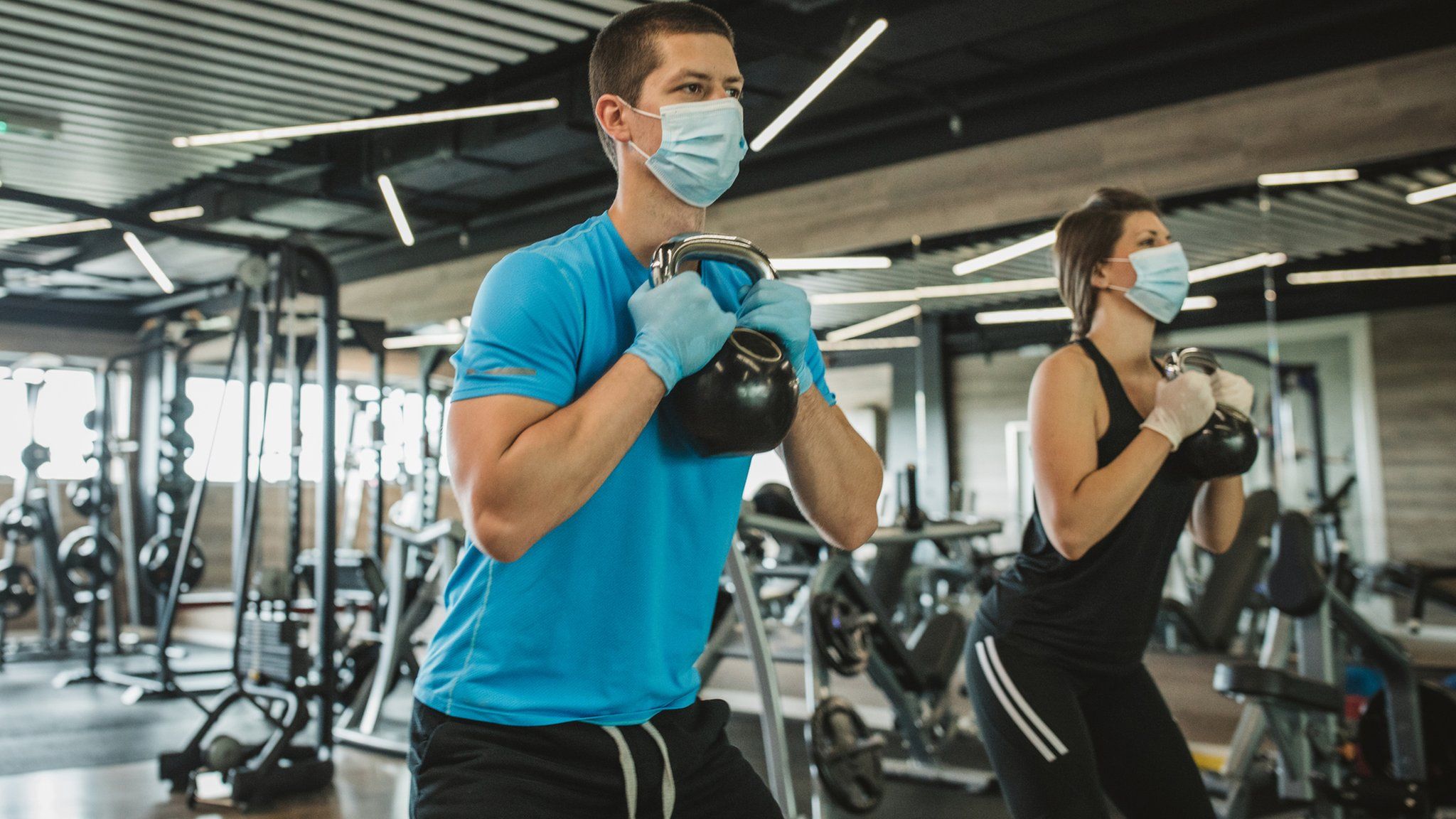 Man and woman wearing masks working out at a gym