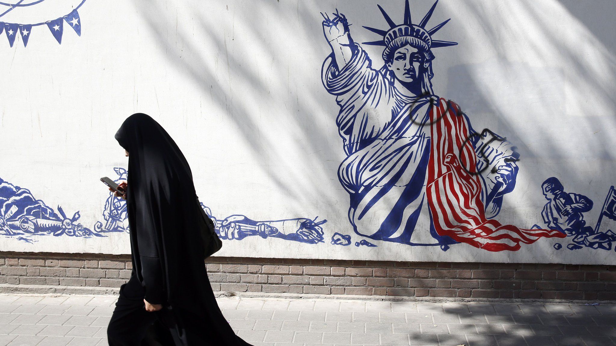 File photo showing an Iranian woman walks past an anti-US mural in Tehran, Iran (16 August 2023)