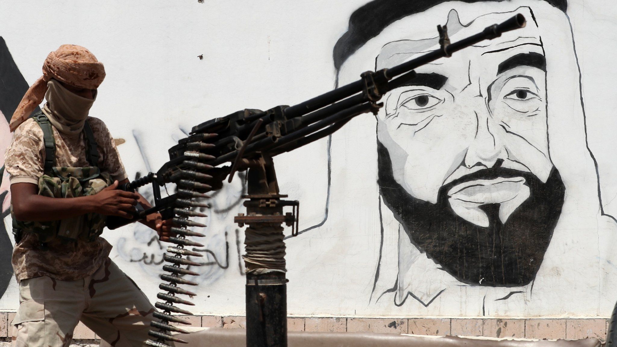 UAE-backed Yemeni pro-government fighter mans a machine-gun next to a mural in Mukalla showing the UAE's late founder and president, Sheikh Zayed bin Sultan Al Nahyan (8 August 2018)