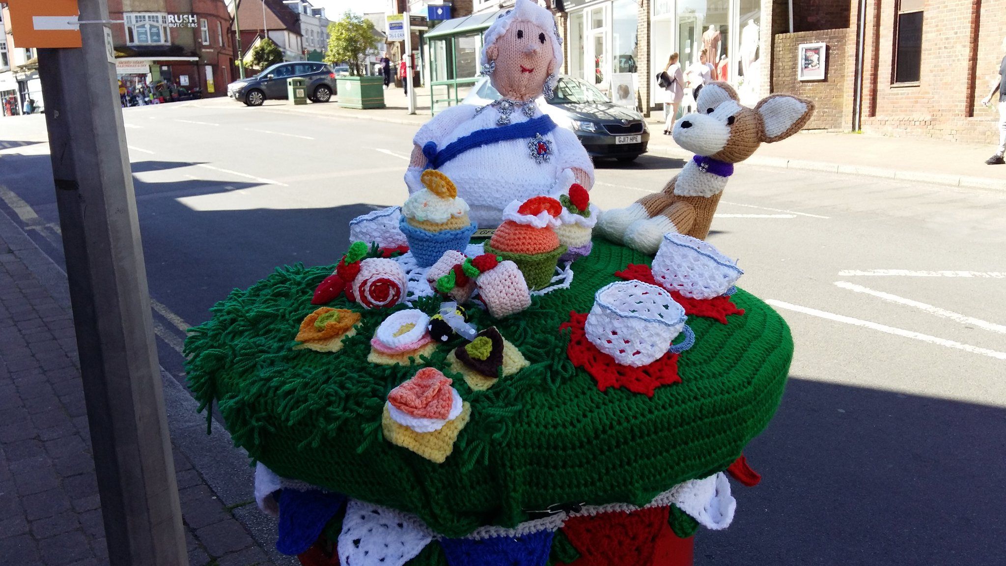 A knitted post box topper showing the queen, a corgi and cakes in Crowborugh
