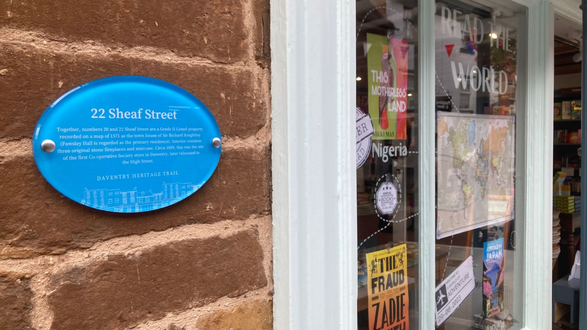 Brick wall with blue plaque alongside windows of a book shop, featuring map and various event posters