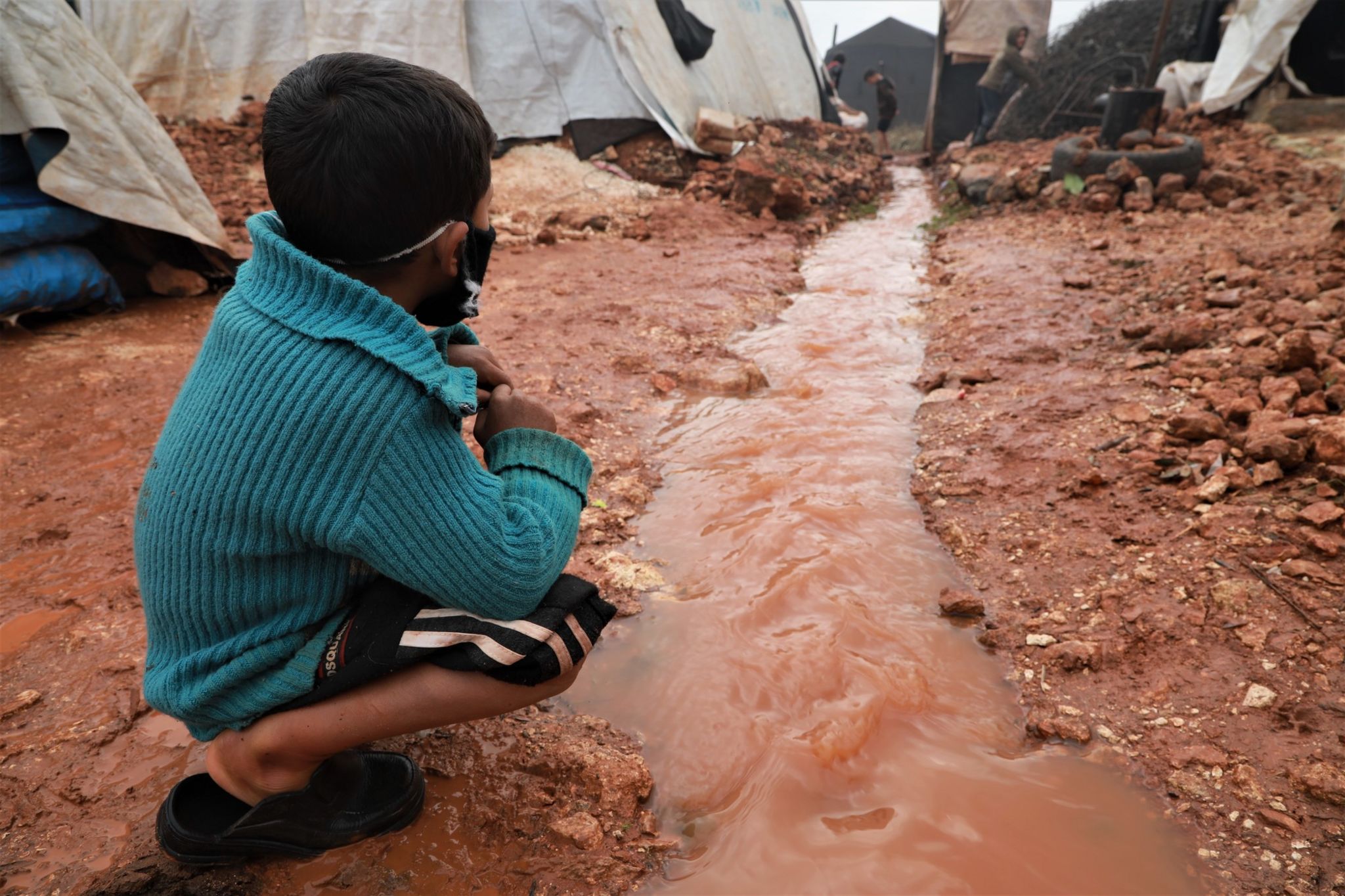 A boy looks at a water channel through a camp for displaced people in north-western Syria