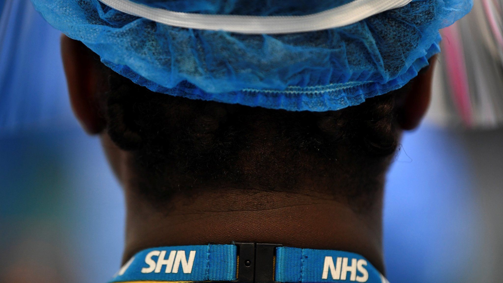 Healthcare worker wearing an NHS lanyard seen from behind