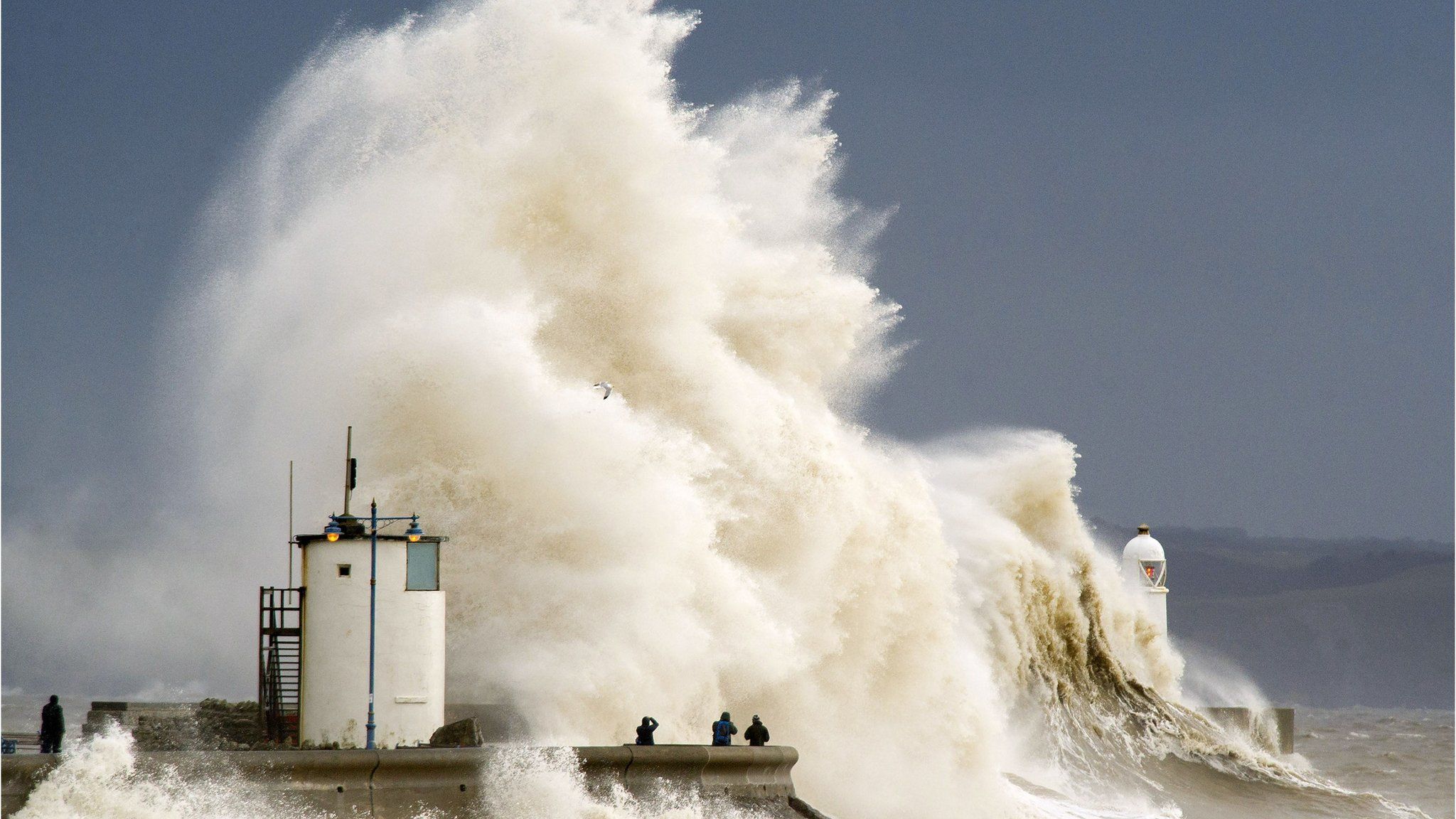 Spectators watch as waves break over the harbour wall at Porthcawl