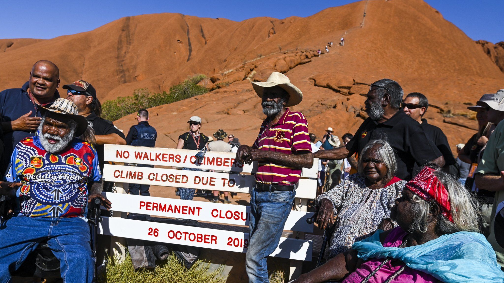 Traditional owners pose for photographs next to the newly installed sign after the permanent closure of the climb at Uluru