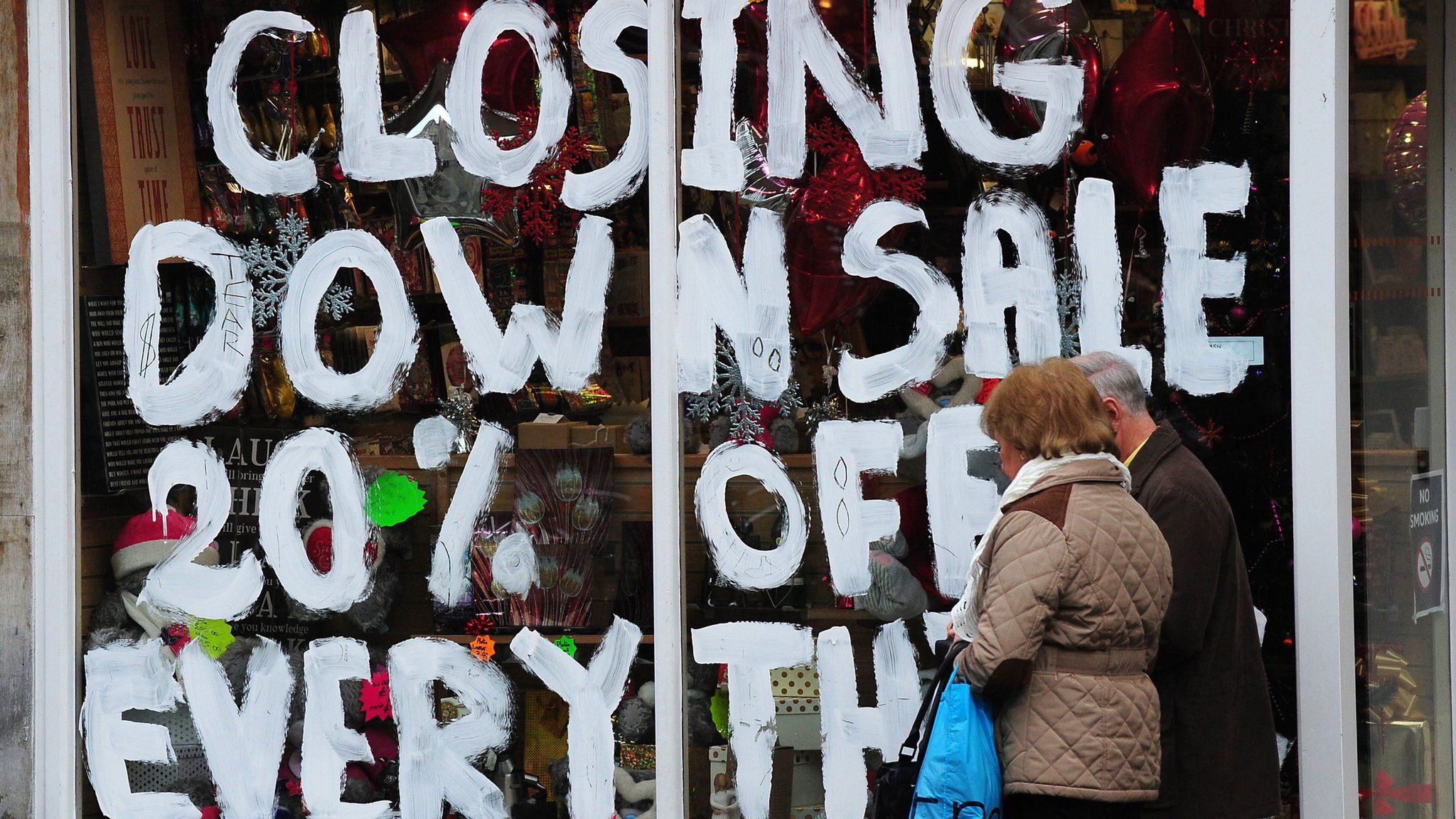 ;'losing Down 20% off everything' on shop window with two people walking past