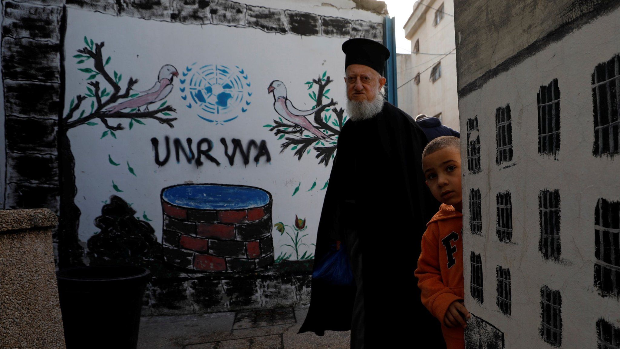 Palestinians stand near a mural showing the logo of United Nations Relief and Works Agency (Unrwa) in Jalazone refugee camp, near the West Bank city of Ramallah (3 January 2018)